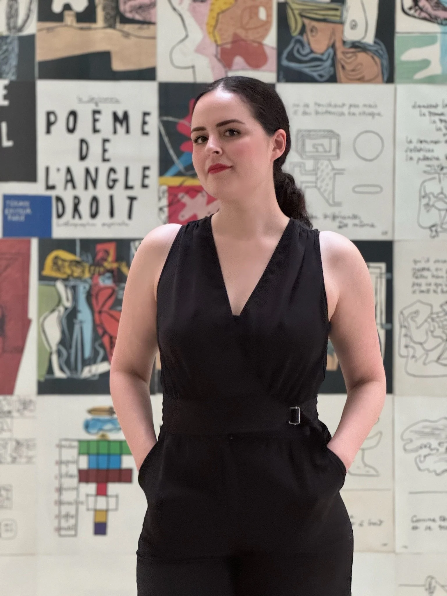 Mujer de cabello oscuro y vestido negro frente a un mural colorido con ilustraciones y texto.
