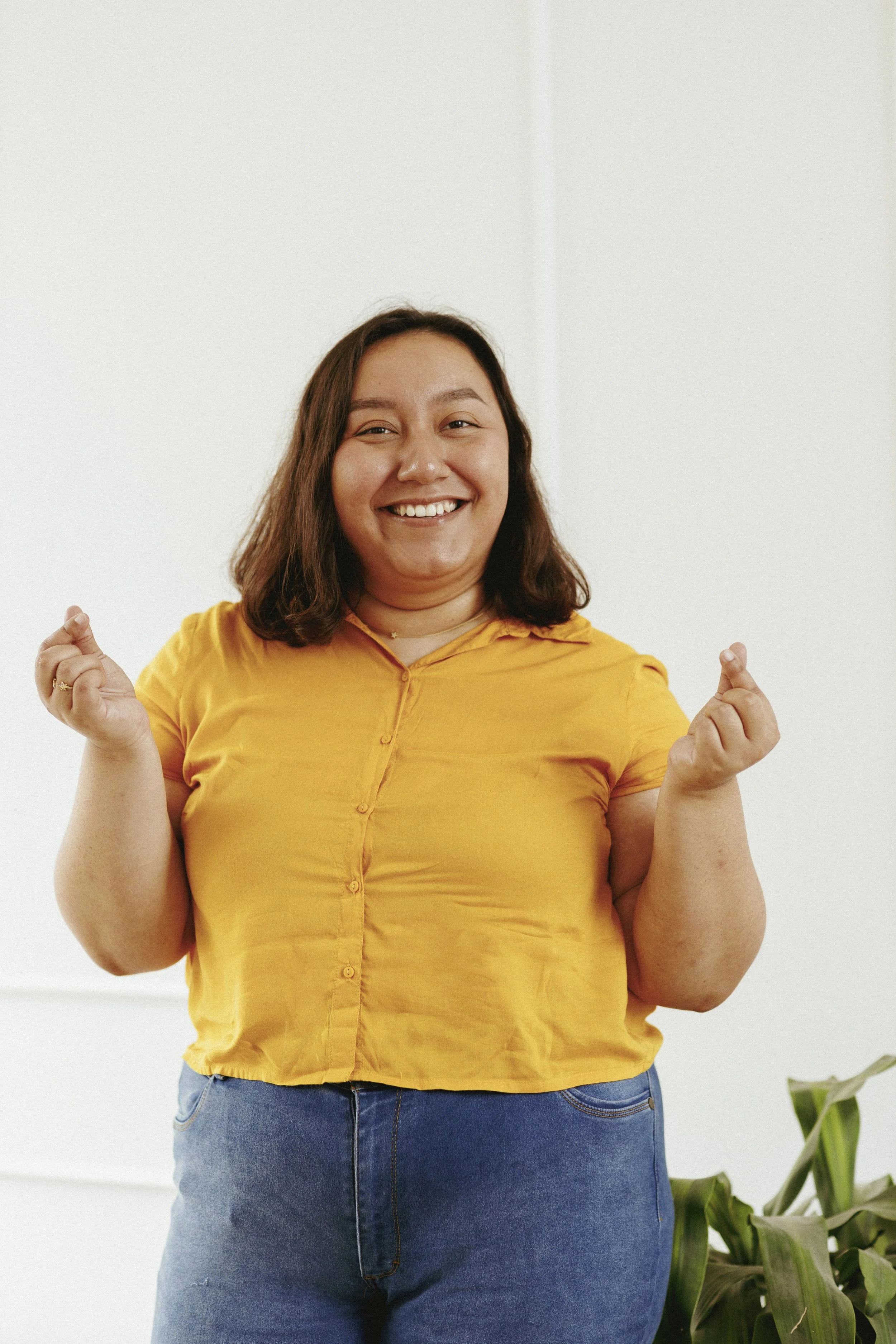 Persona sonriendo, vistiendo una camisa amarilla y pantalones de mezclilla, con las manos levantadas en un gesto positivo.