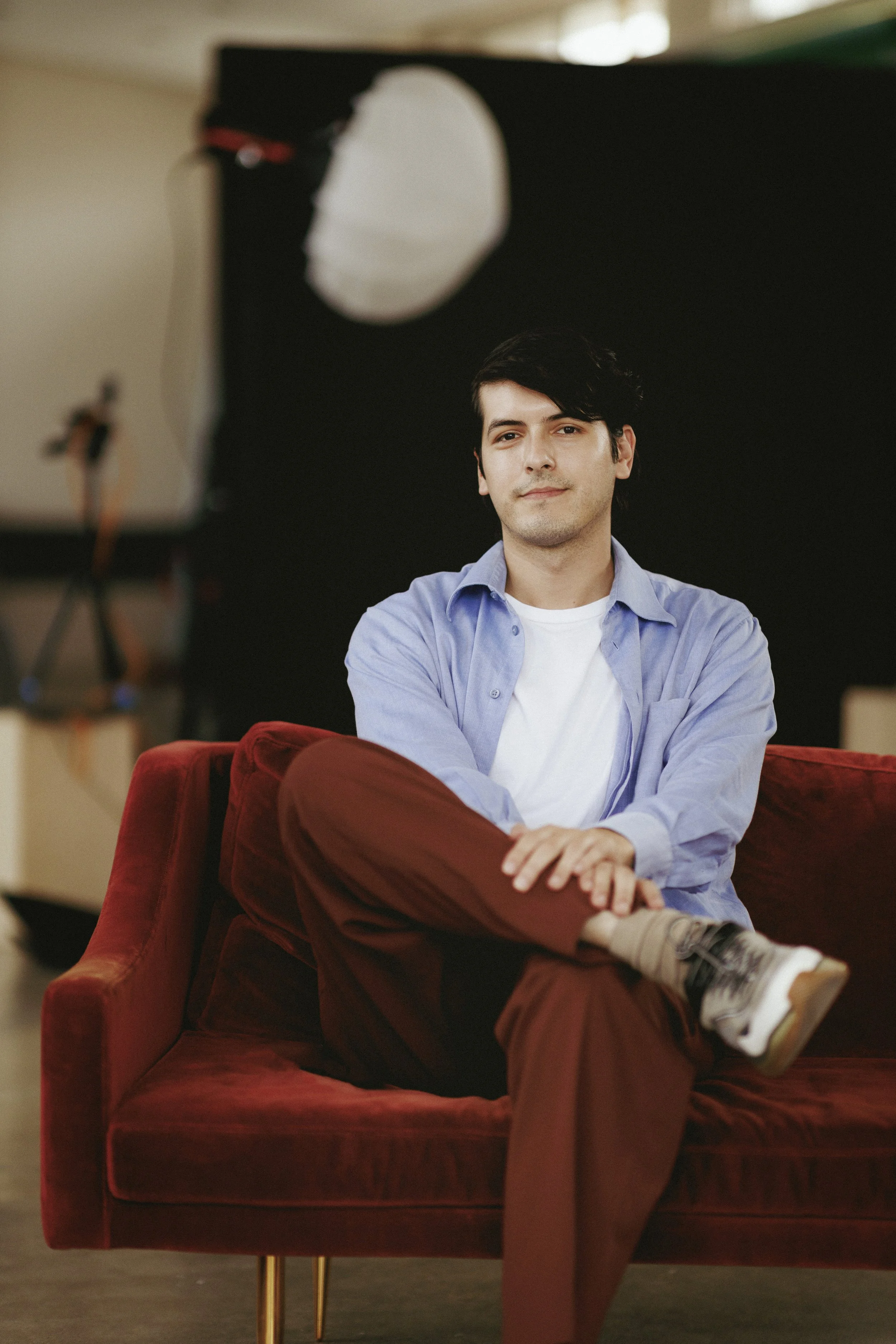 Hombre sentado en un sofá rojo con fondo negro en estudio de fotografía.