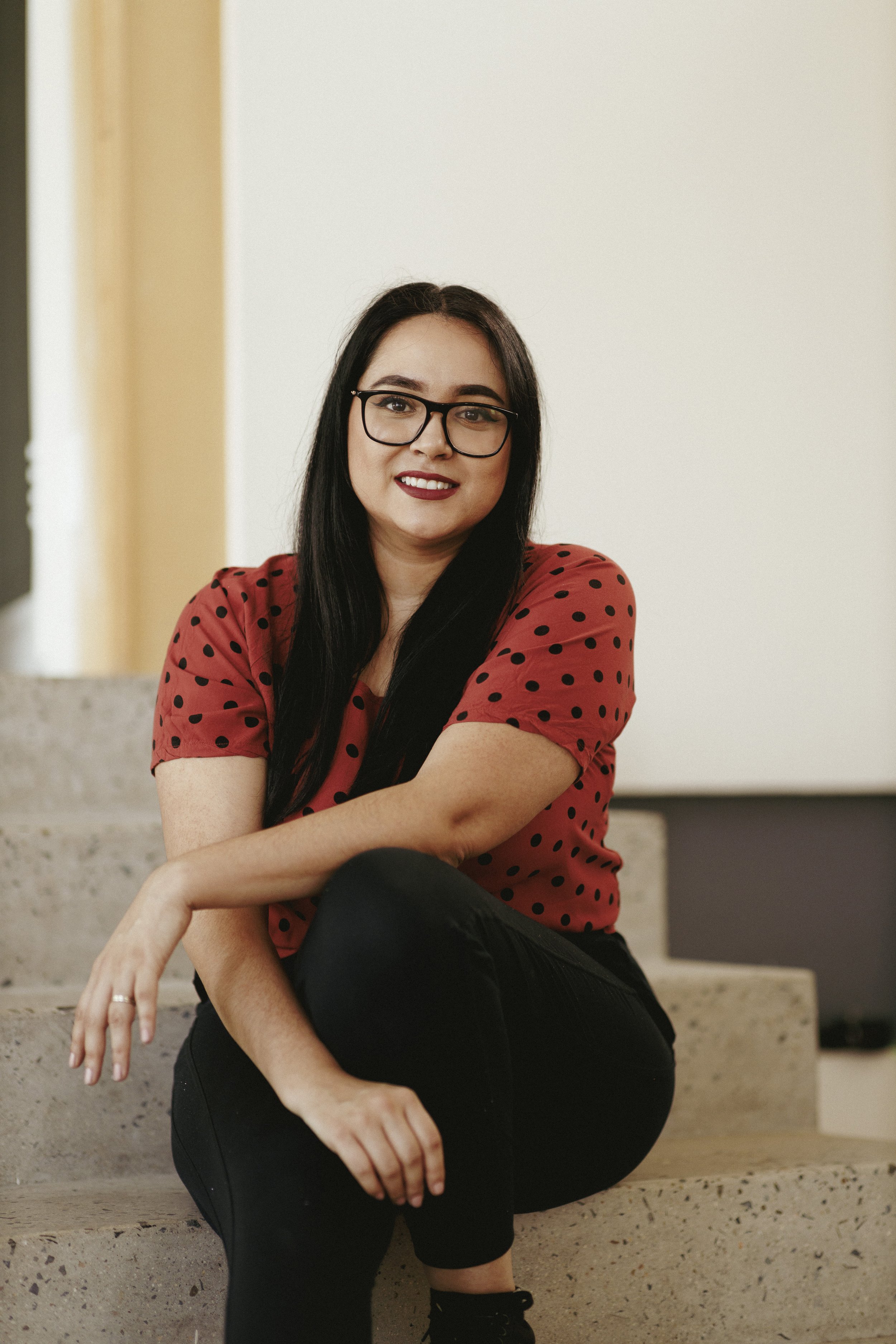Persona sentada en escaleras con camisa roja de lunares y gafas.