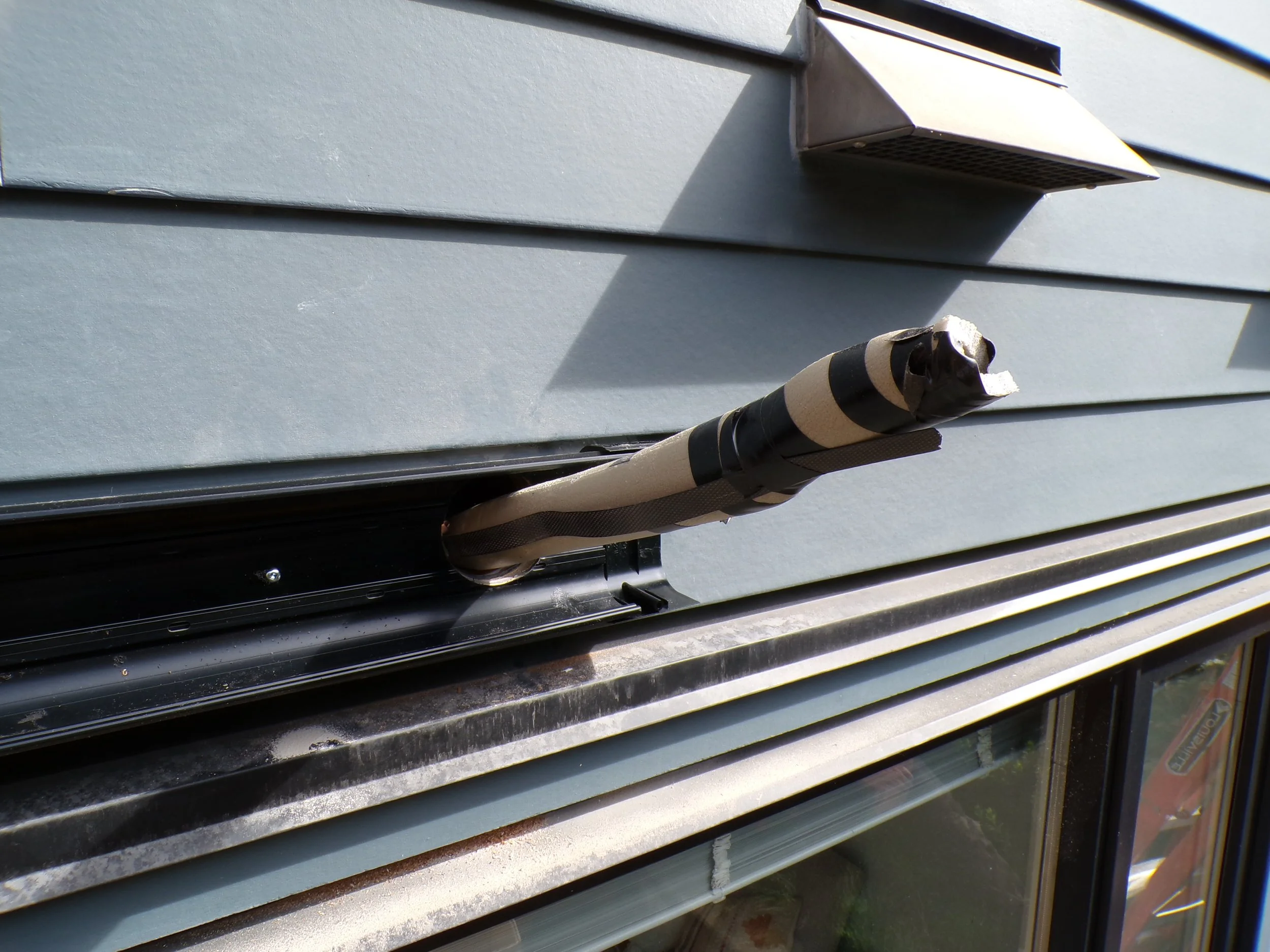 Close-up of an air vent or exhaust pipe on the exterior of a building, with protective tape partially removed.
