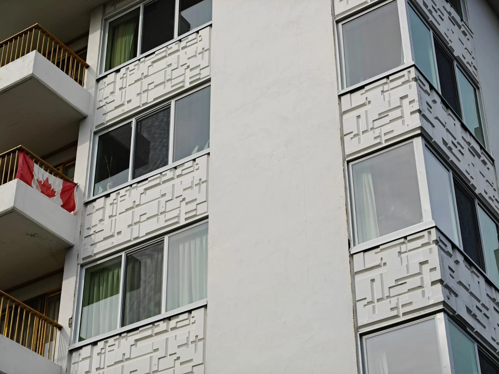 Front view of a multi-story white apartment building with balconies and large windows, parking lot with cars, and a person walking outside.