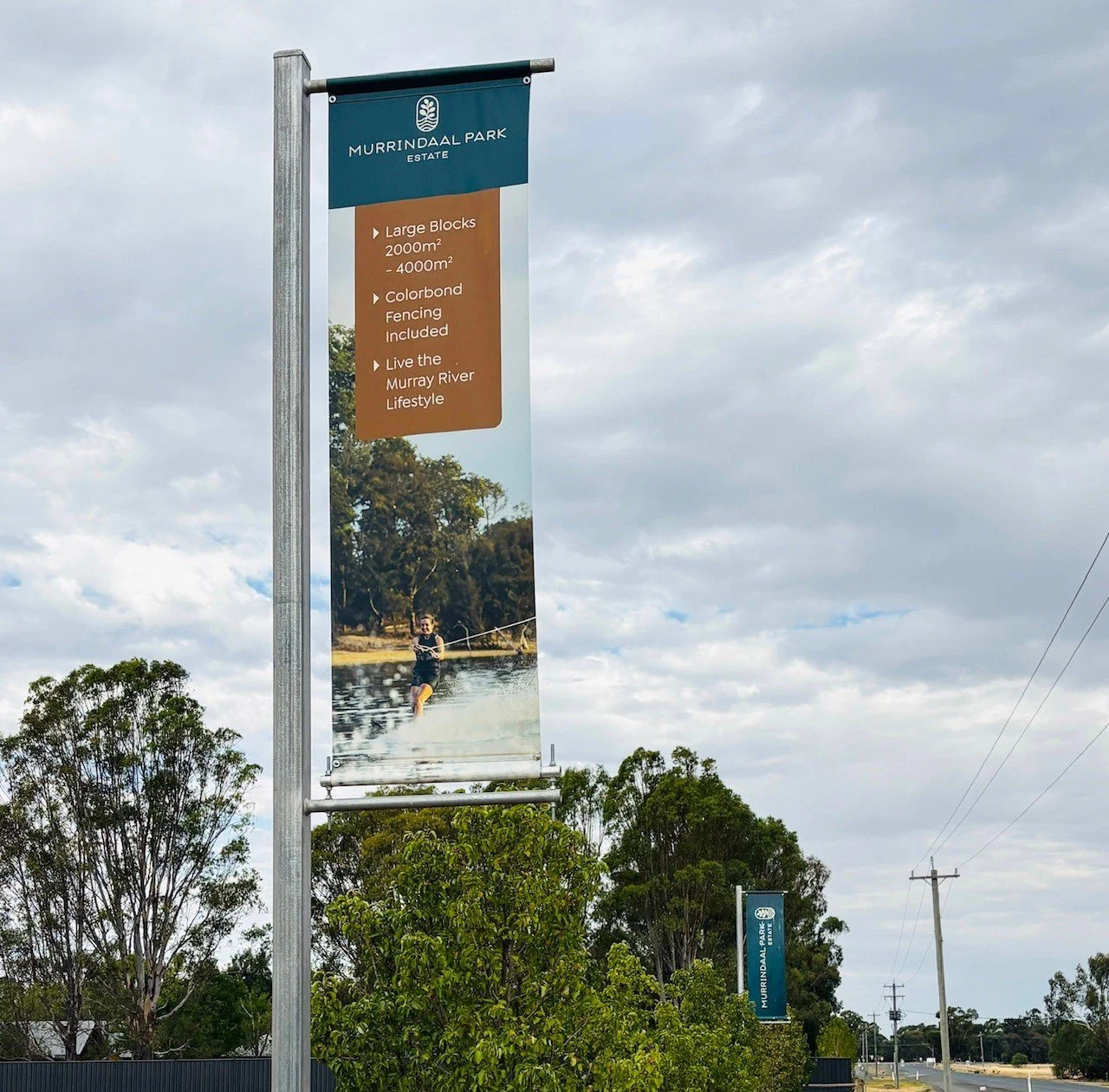 A vertical banner for Murrindal Park Estate with details about large blocks for sale, fencing inclusion, and river lifestyle, featuring a person wakeboarding on a river, with trees and a cloudy sky in the background.