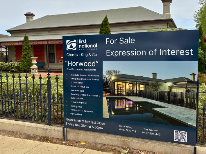 A large sign advertising a historic home. The sign includes property details and features a photo of the house's backyard with a pool. The sign also displays the real estate agency - Charles L King and Co. 