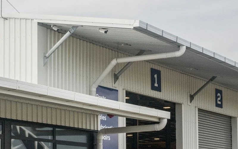 Close-up of the exterior of a building with two large garage doors labeled '1' and '2', white corrugated metal siding, and white drainage pipes attached to the facade.