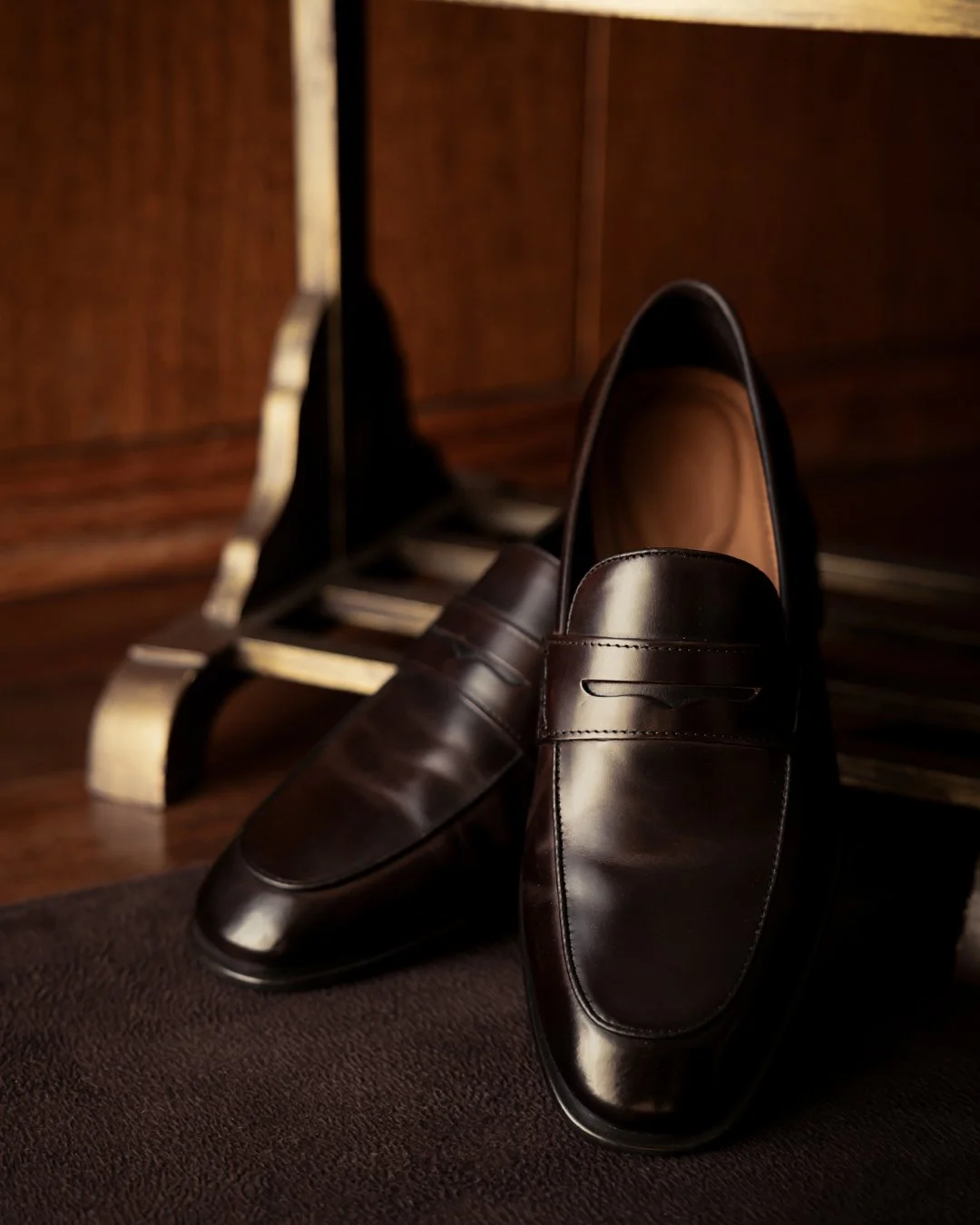 Sapatos sociais masculinos pretos de couro, colocados sobre uma superfície escura com fundo de móveis de madeira.