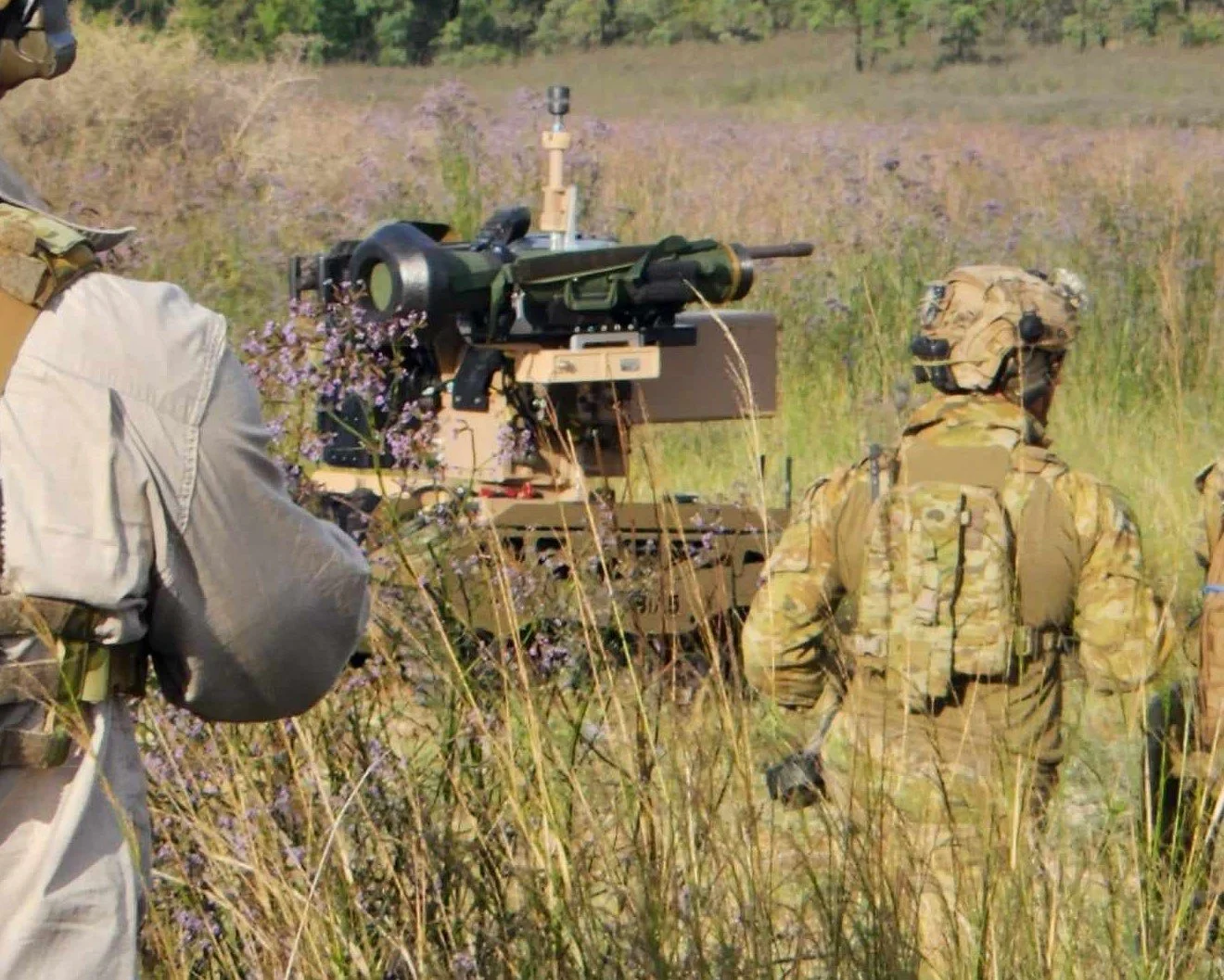 Soldiers in camouflage uniform operating a military weapon in a grassy field.