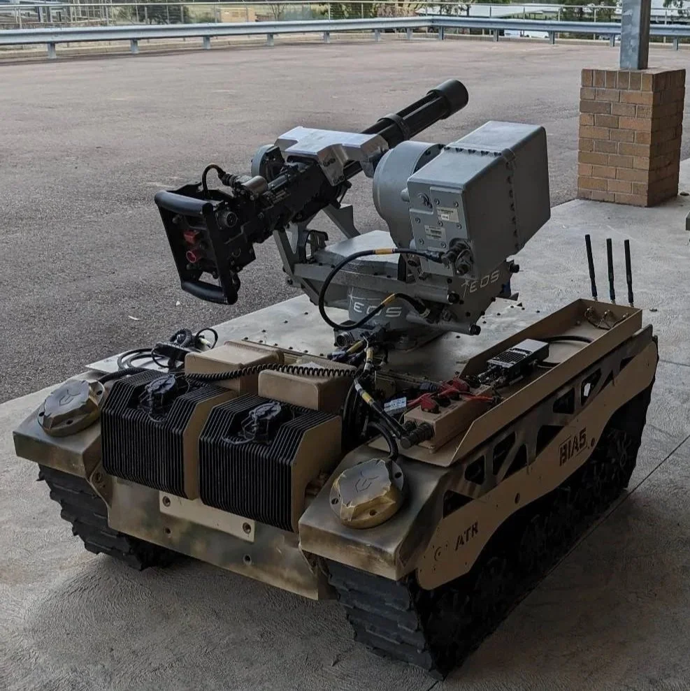 A robotic military vehicle with a mounted weapon system, tracked wheels, and electronic components, positioned on a concrete surface outdoors.