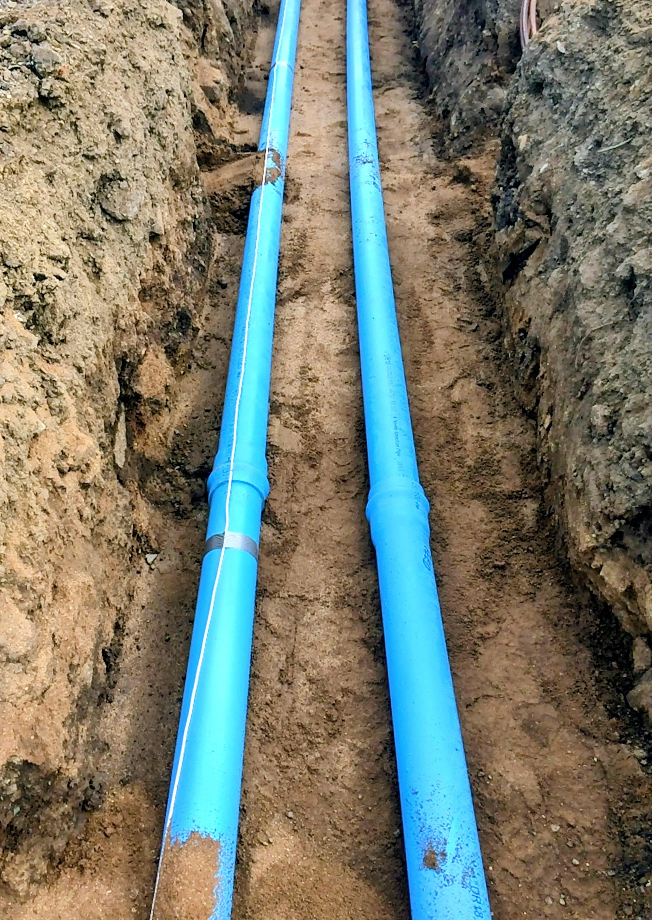 Two blue pipes installed in a trench underground for plumbing or utility purposes.