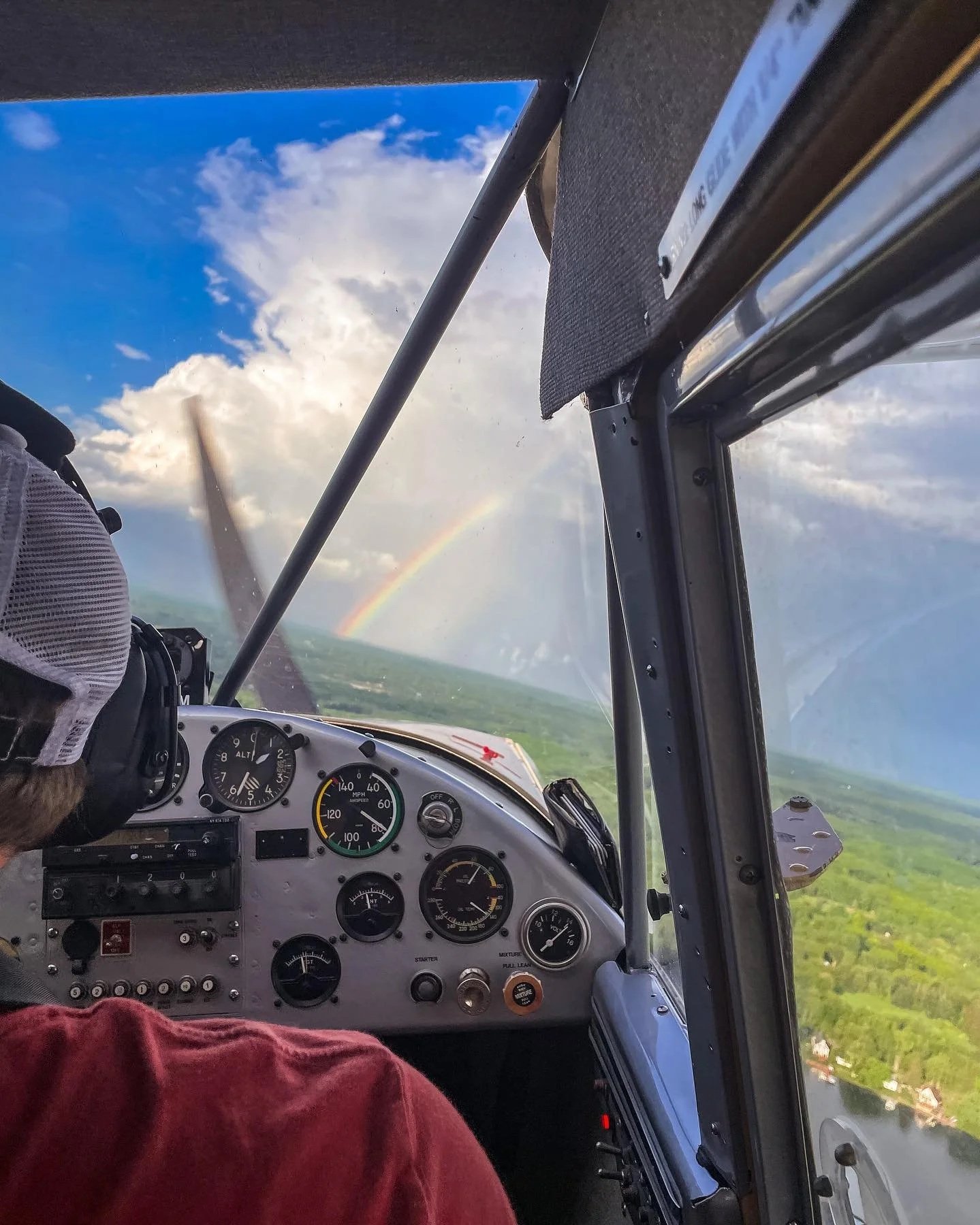 Cockpit view from inside a seaplane flying over Michigan with a rainbow in the distance