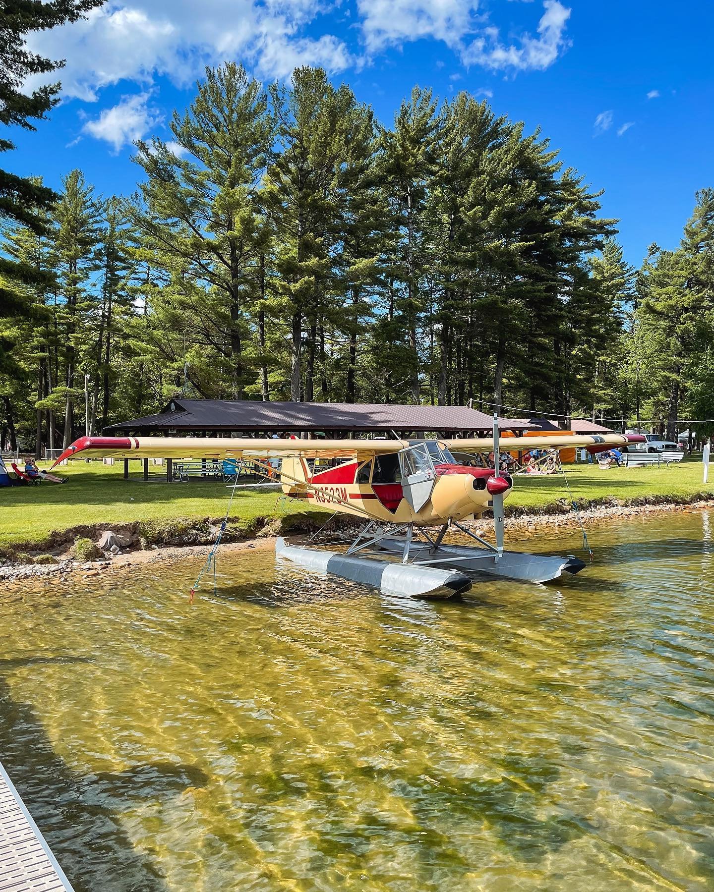 Piper seaplane moored on a clear Michigan lake surrounded by pine trees