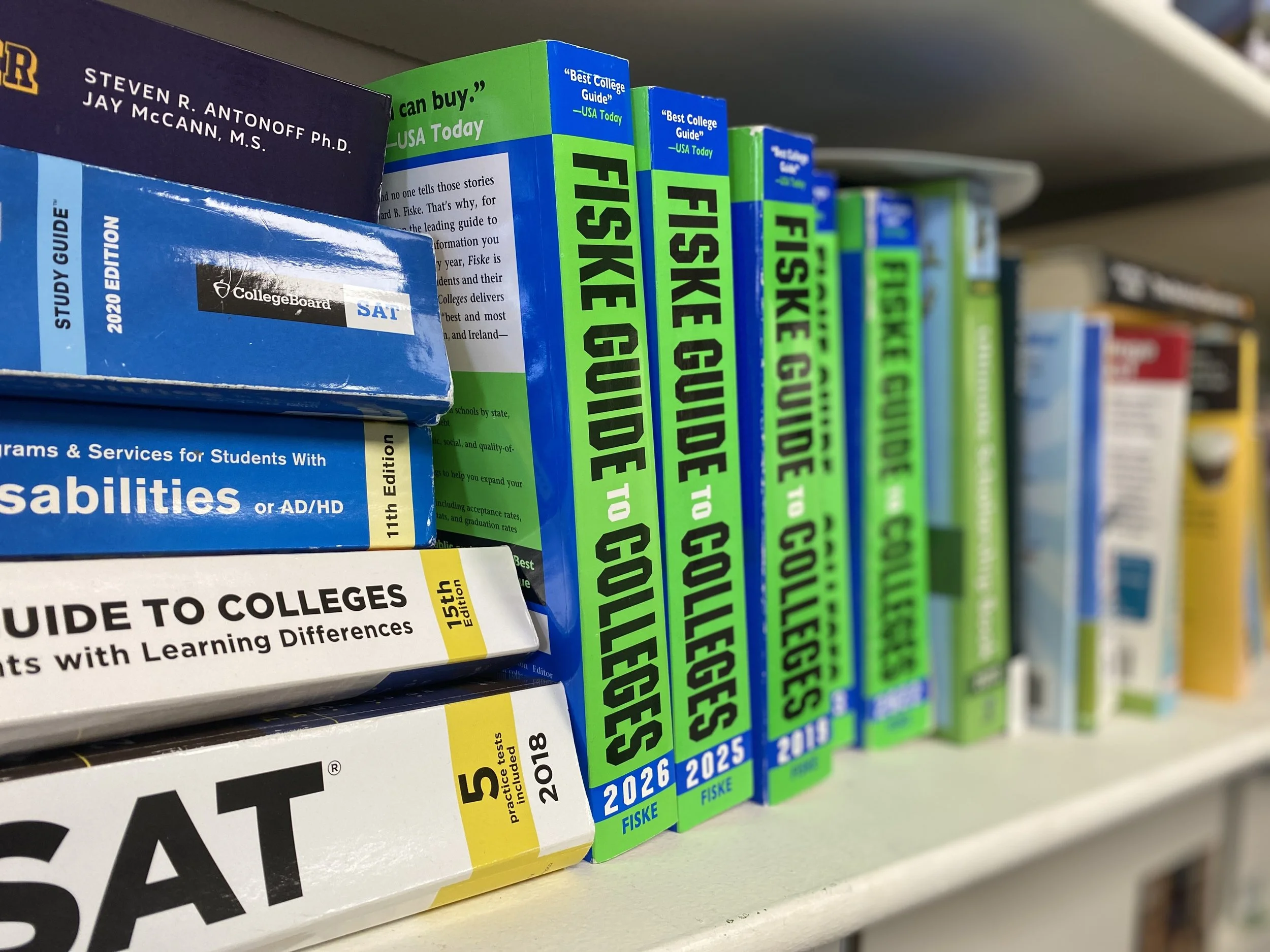 Books about college planning and test preparation arranged on a bookshelf, including 'Fiske Guide to Colleges,' 'SAT,' and 'Disabilities' guides.