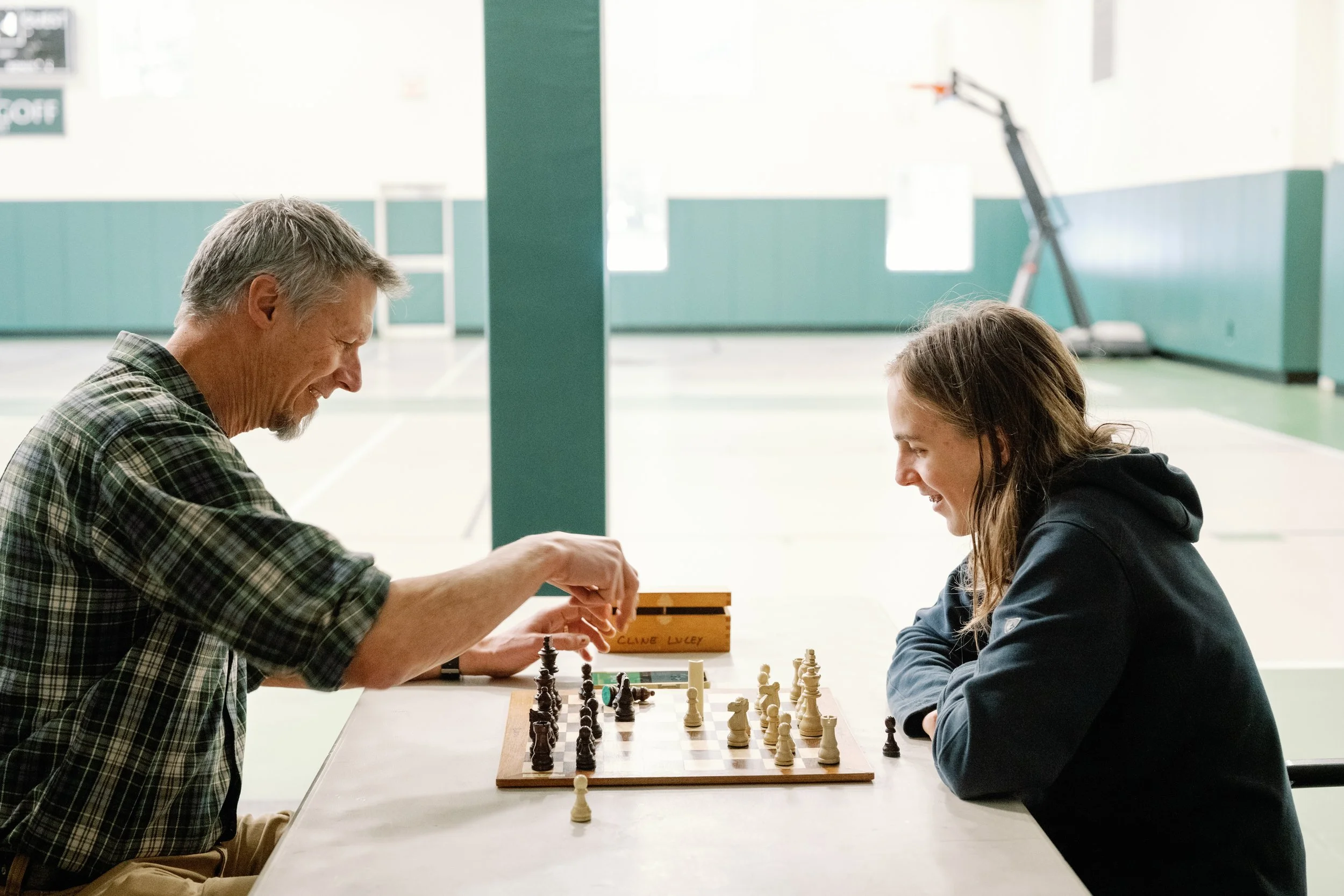An older man and a young girl playing chess at a table in a gymnasium or recreation center.