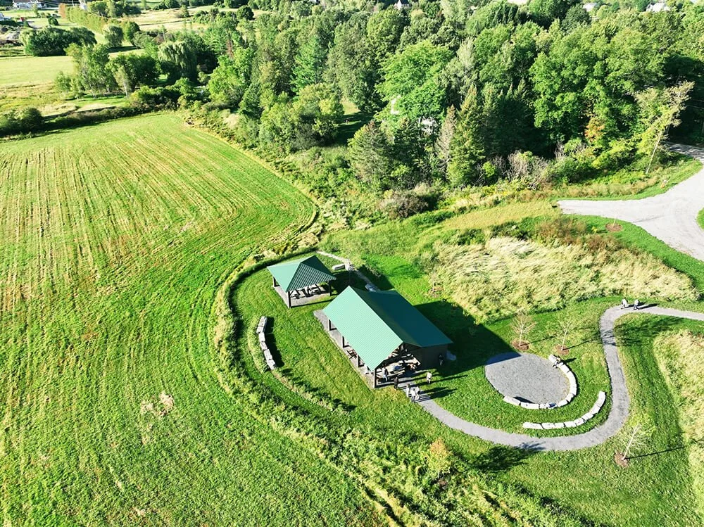 Aerial view of a green lawn area with two buildings with green roofs surrounded by trees and a small circular gravel pathway with benches.