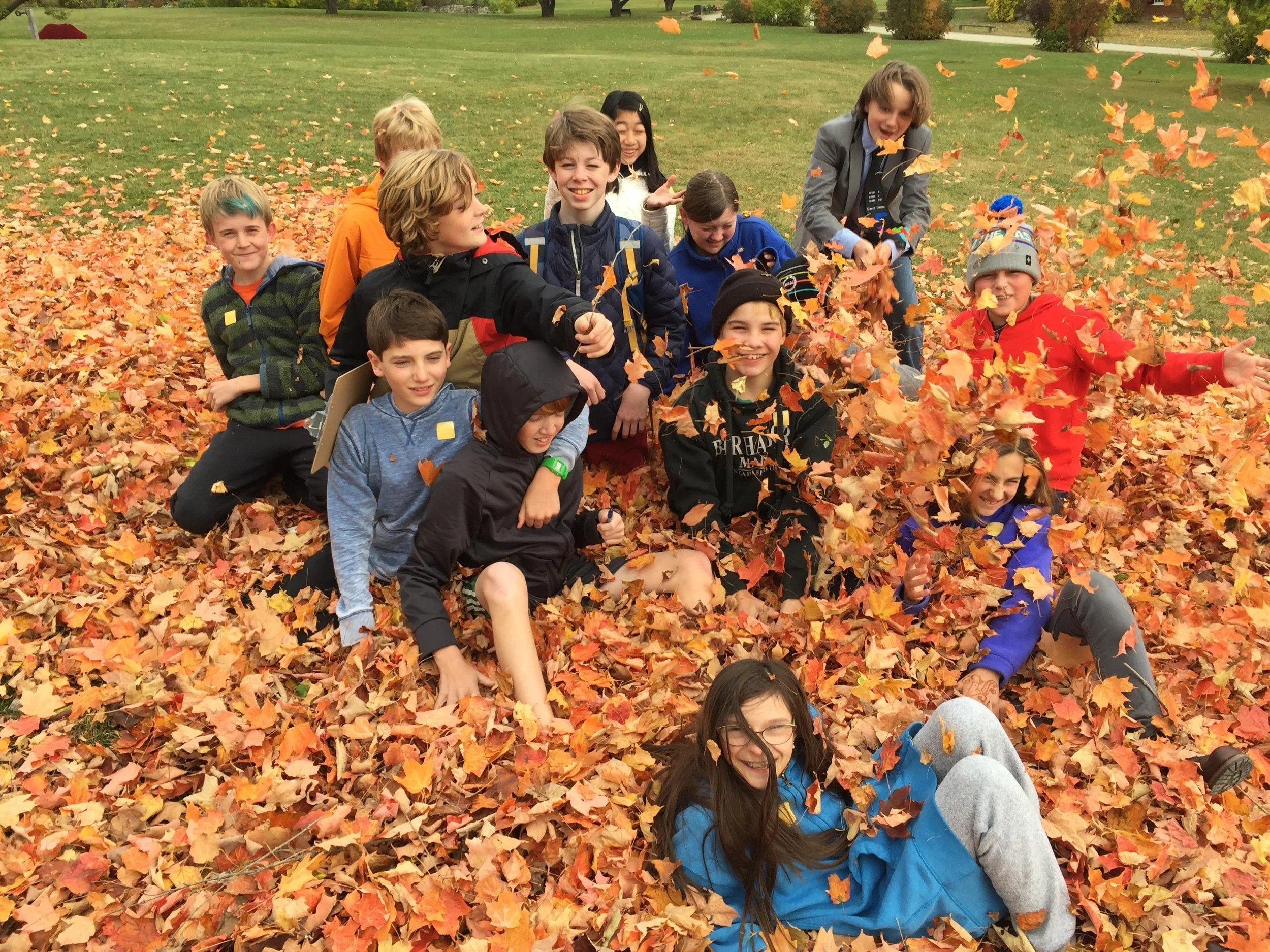Group of kids playing in a pile of colorful autumn leaves in a park.