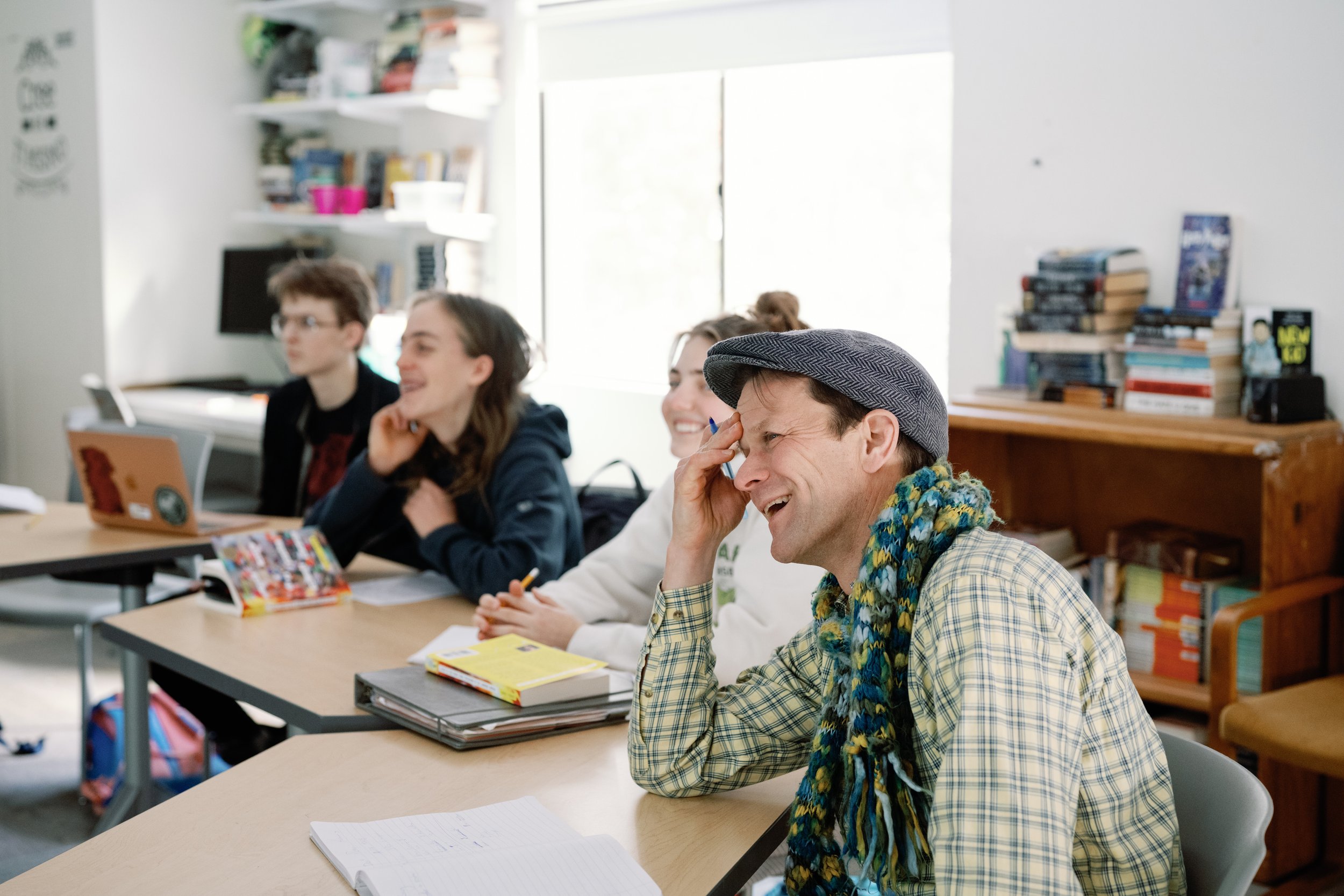 Group of students sitting at desks in a classroom, smiling and laughing during a lesson.