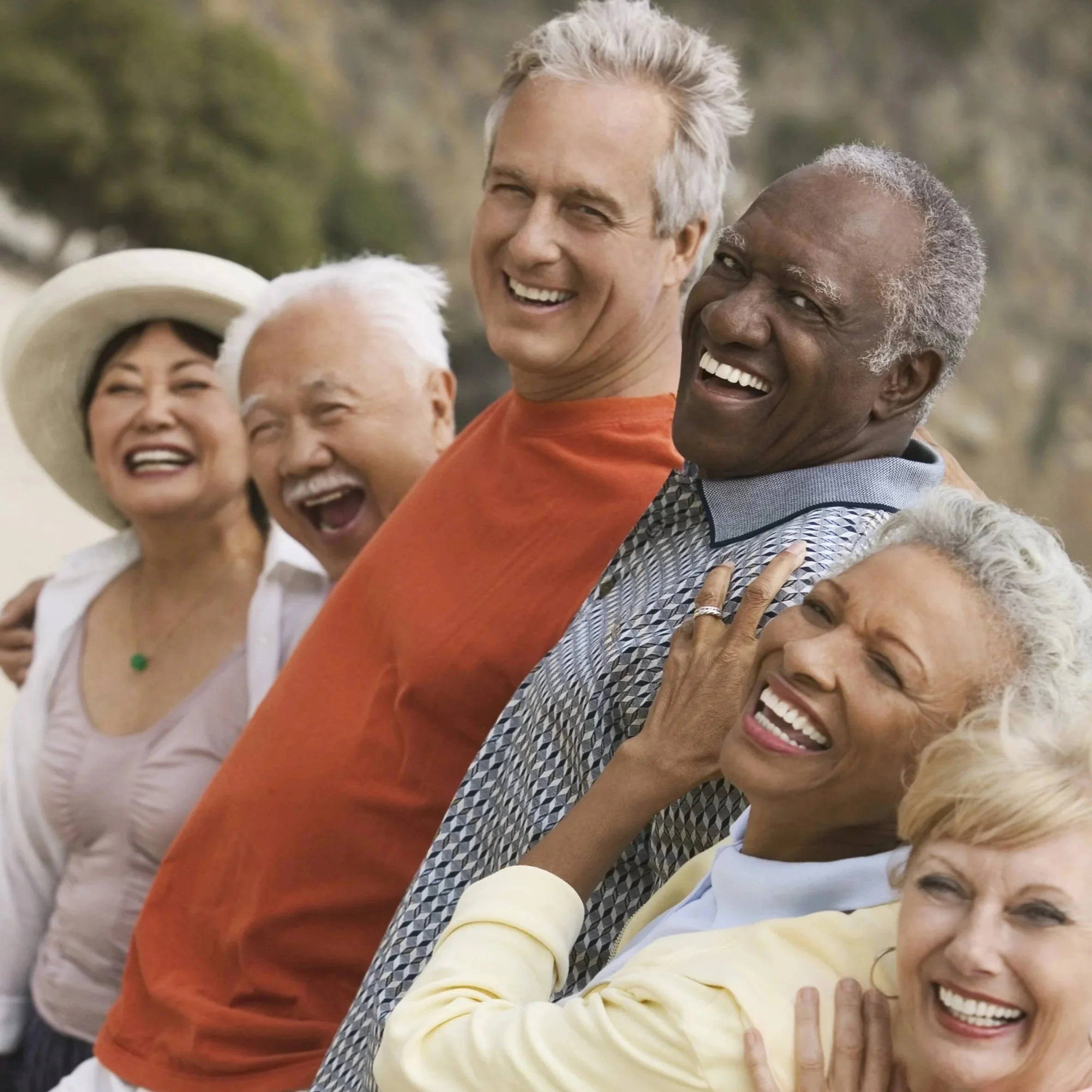 Smiling diverse group of six people outdoors, standing close together and leaning back with arms around each other, enjoying a sunny day.