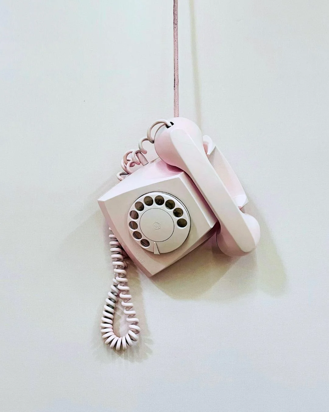 A vintage pink rotary telephone hanging on a plain white wall.