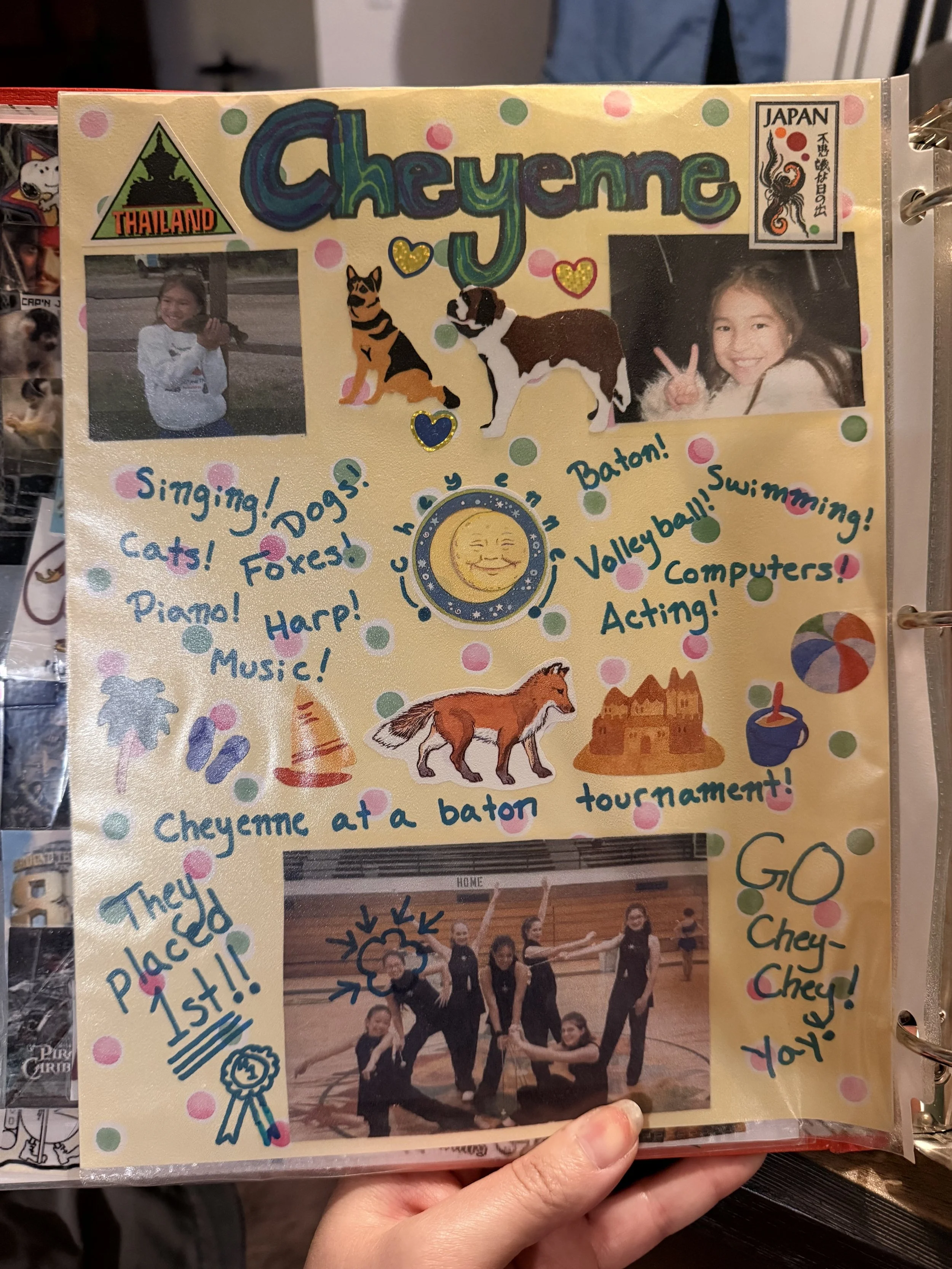 A scrapbook page features two photographs of children, decorative stickers of dogs, cats, a fox, and a cheyenne symbol, along with colorful handwritten notes about various activities like singing, dogs, and basketball. The page has a yellow background with polka dots and a moon illustration.