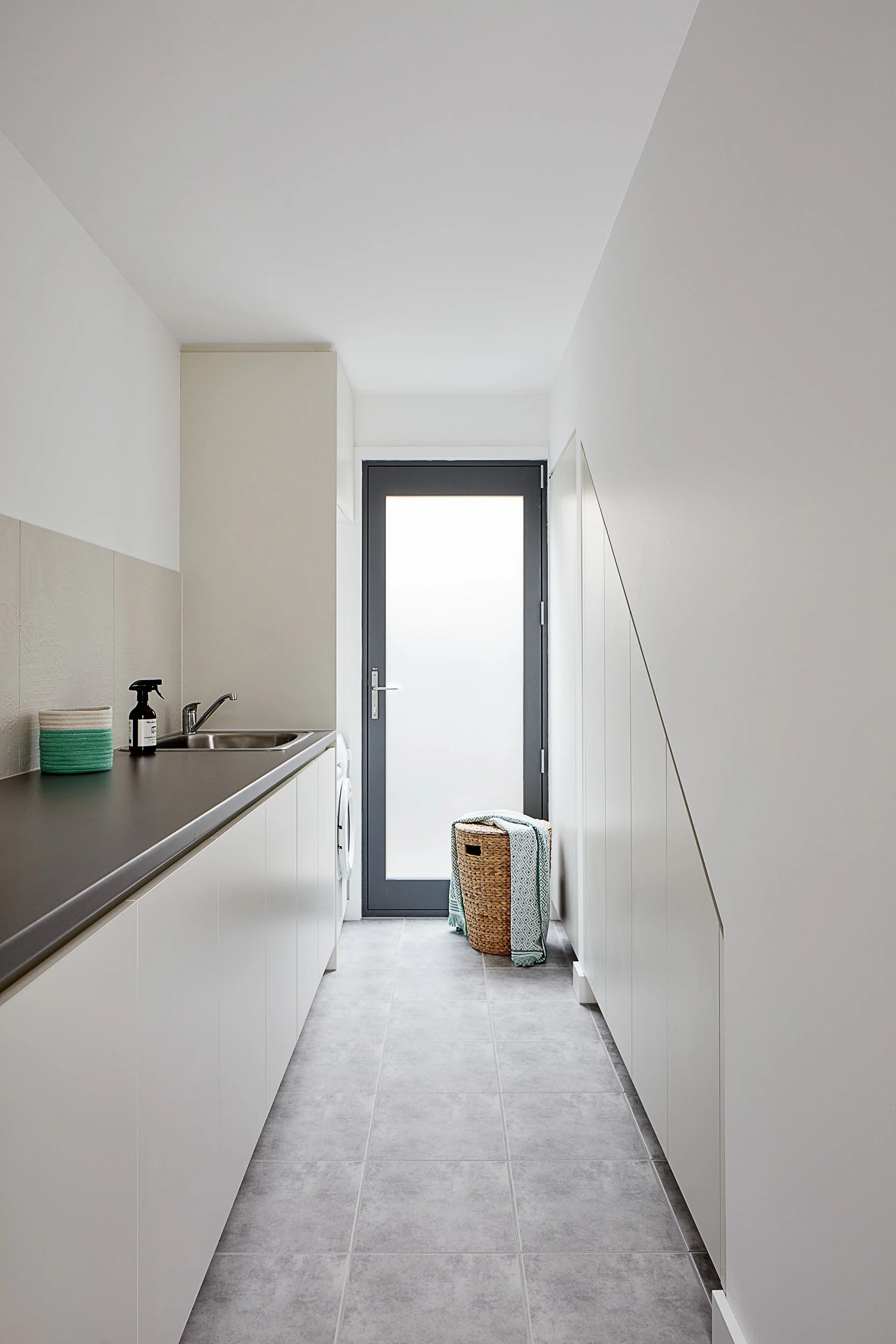 A white + grey tiled laundry space with a swing door 