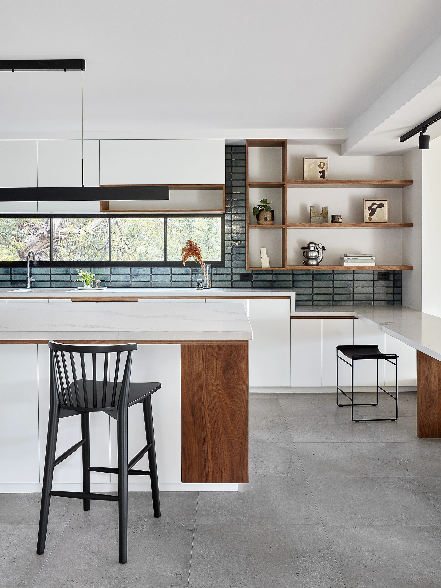 Modern kitchen with white cabinets, black subway tile backsplash, wooden shelves, and a black bar stool.