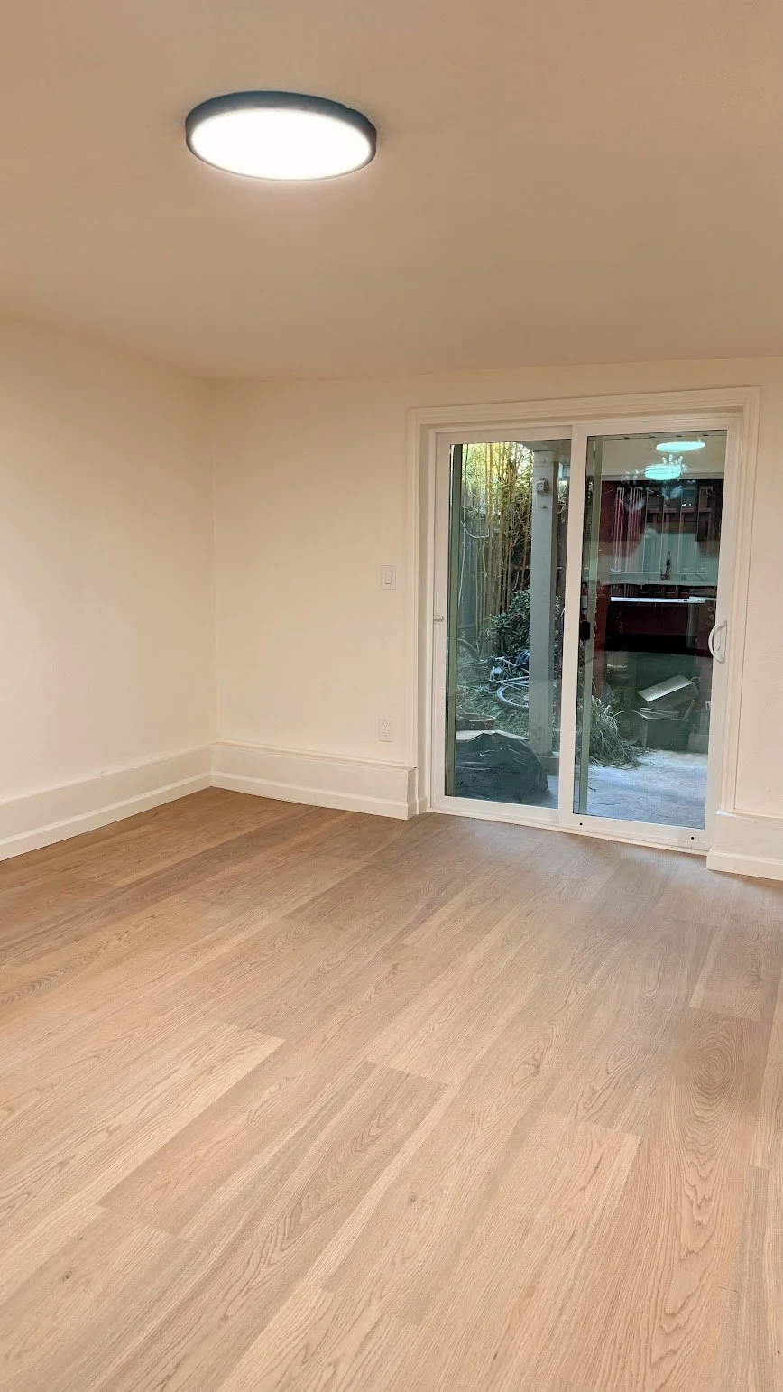 Empty room with wooden flooring, cream-colored walls, ceiling light, and a sliding glass door leading to an outside area.