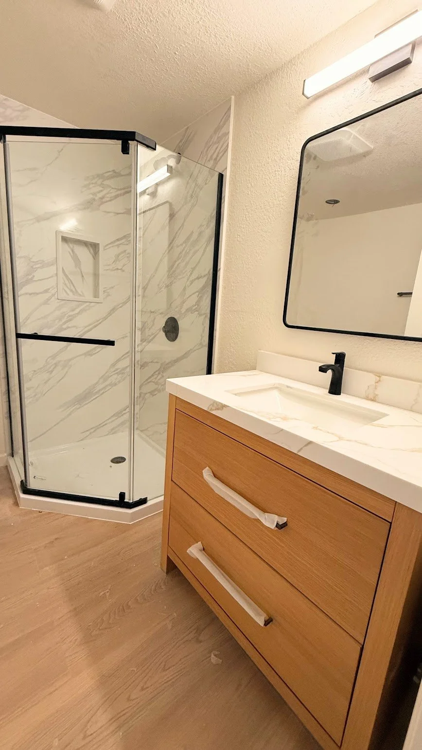 A modern bathroom with a glass shower enclosure, a white marble vanity with a black faucet, and a large rectangular mirror on the wall.