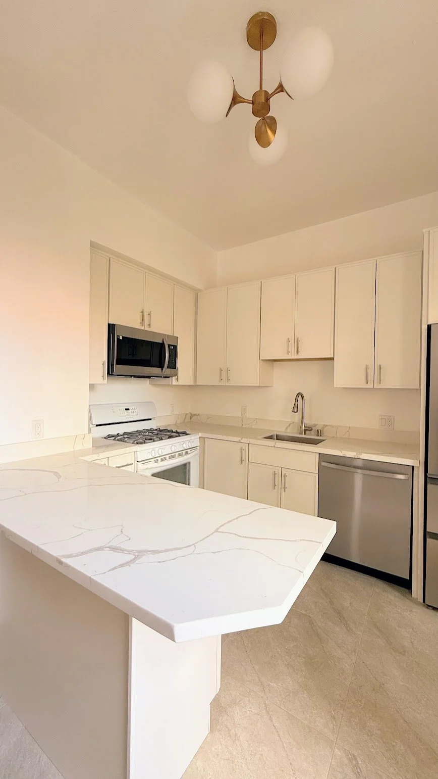 Modern kitchen with white cabinets, marble countertops, and stainless steel appliances including a microwave, oven, and dishwasher.