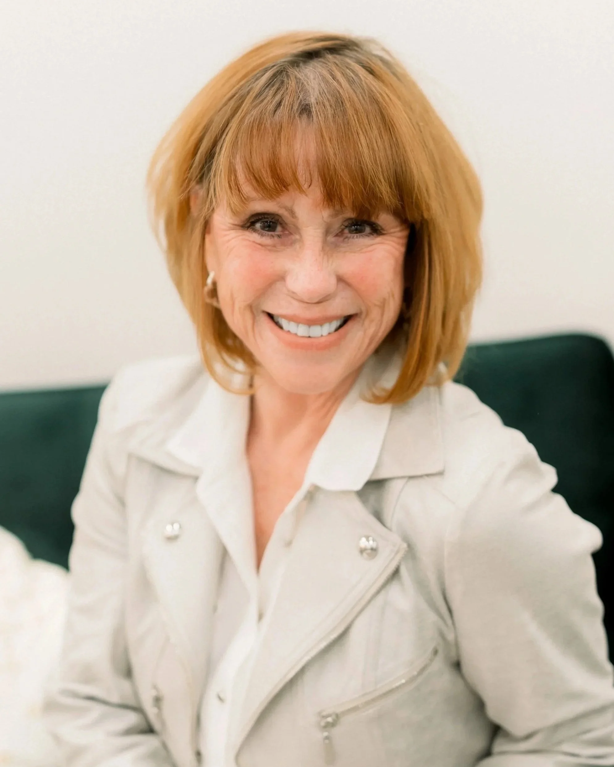 A smiling woman with red hair wearing a white jacket.
