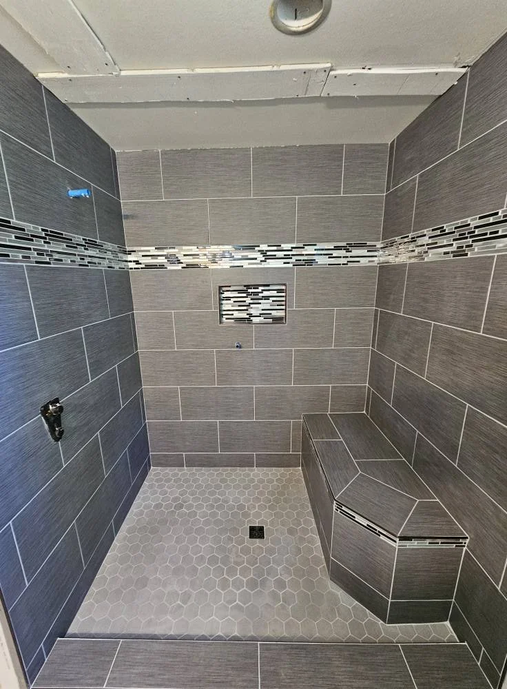 Modern shower with gray tiles, a built-in bench, and a decorative tile strip running horizontally.
