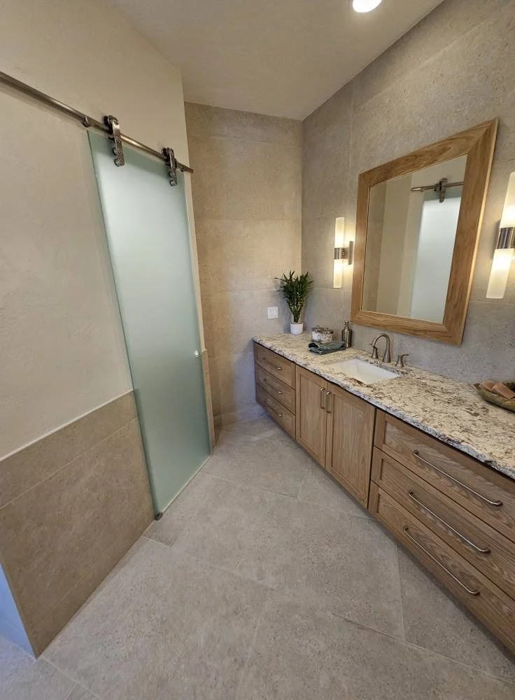 Modern bathroom with a floating vanity with a granite countertop, a large mirror with a wooden frame, a frosted glass shower door with a sliding rail, and wall-mounted light fixtures.