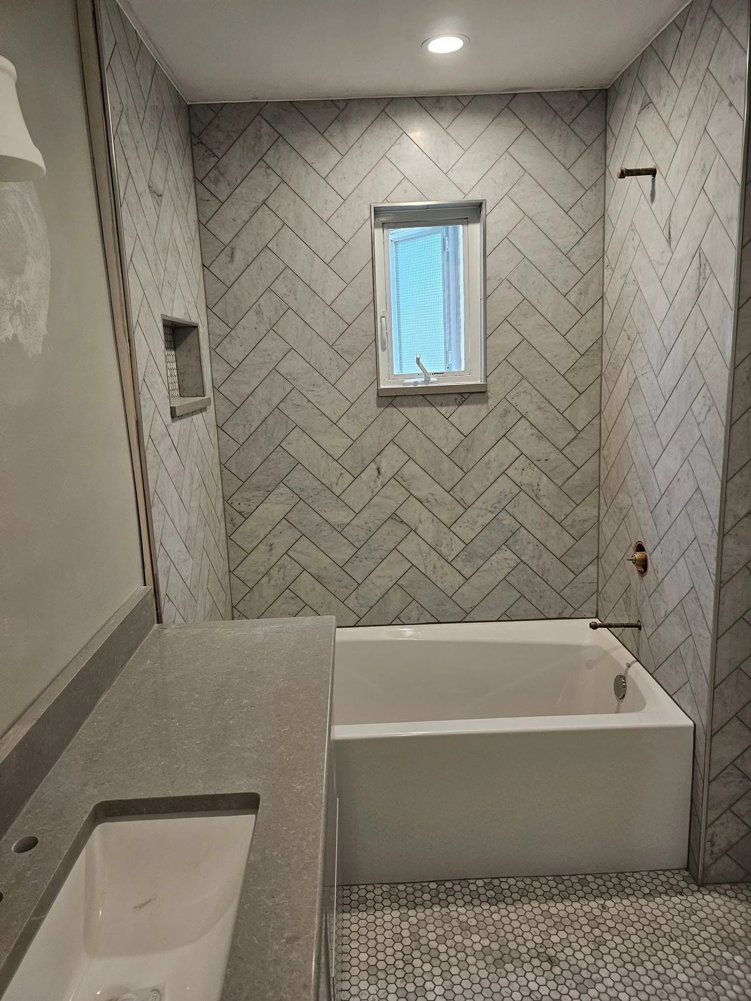 Bathroom with a small window, herringbone patterned tile wall, bathtub, and bathroom vanity with a sink.