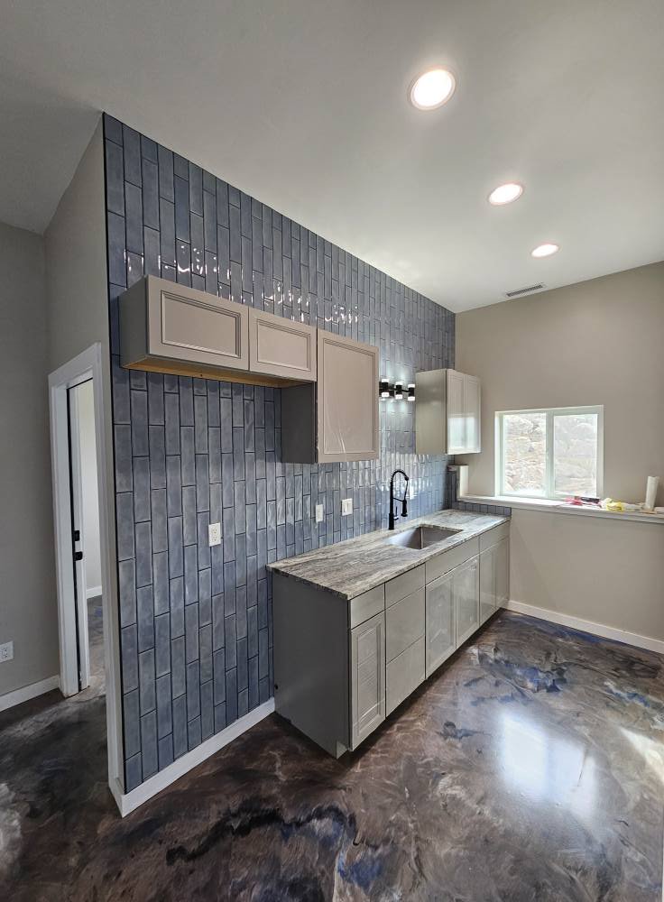 Kitchen with blue tile backsplash, beige cabinets, granite countertop, dark wood floor, and a window with outdoor view.