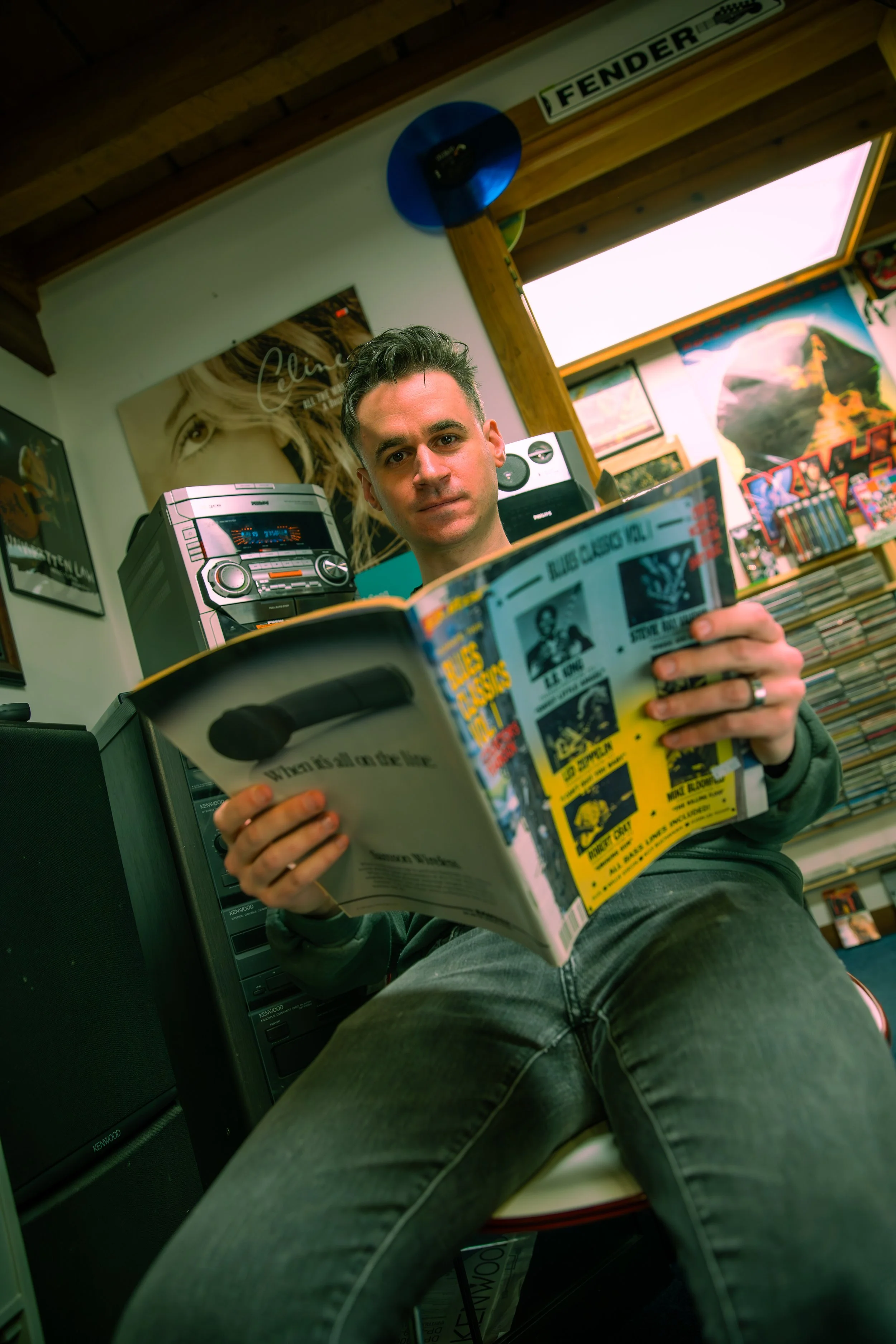 A rugged mountainous landscape with colorful, smooth rocks in the foreground and snow patches on the mountain slopes in the background, under a cloudy sky.