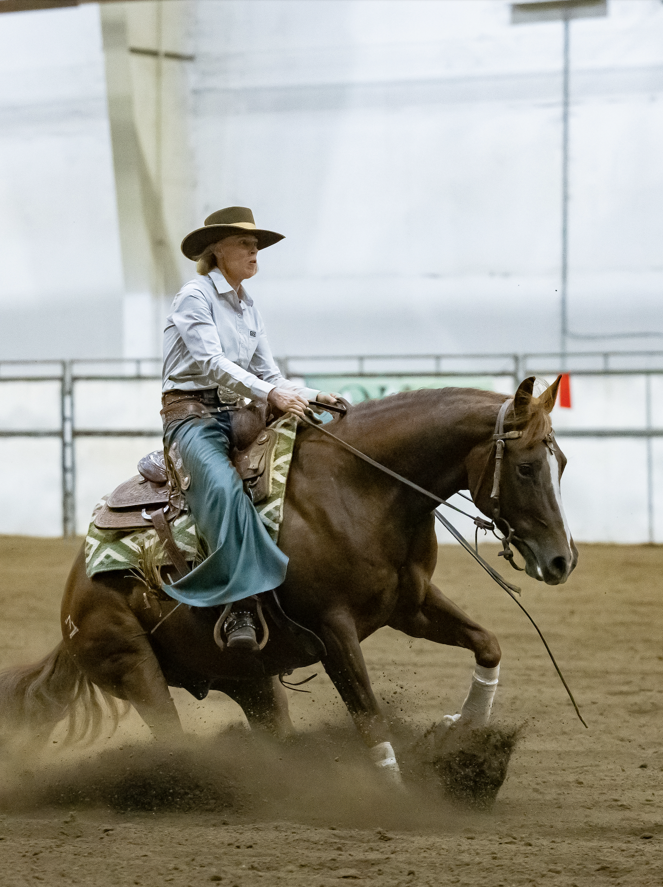 A woman doing a sliding stop a horse in an indoor arena during a cowhorse show.