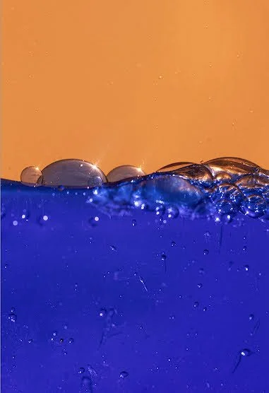 Gotas de agua en la superficie de un líquido de color azul oscuro con fondo anaranjado.
