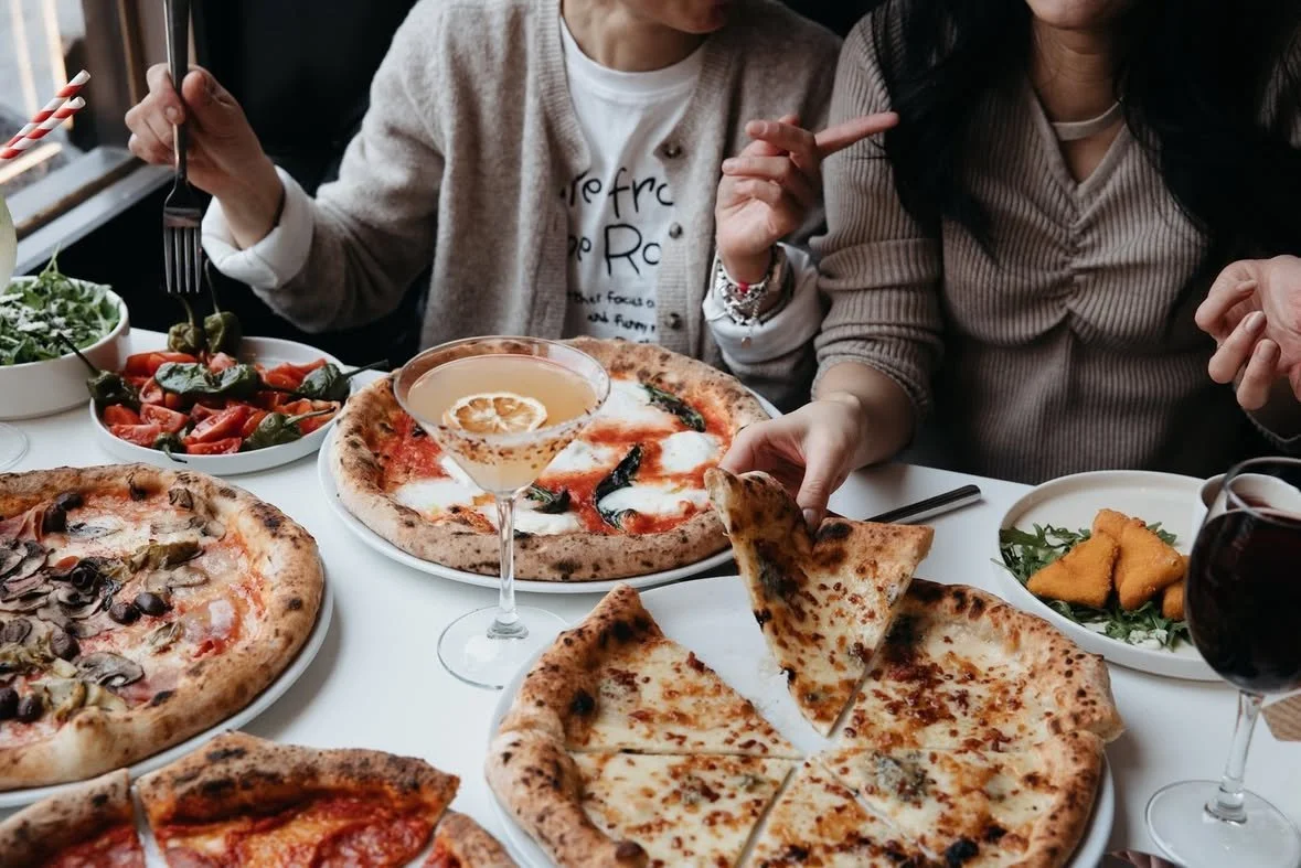 People eating pizza and drinking at a table with salads and drinks.