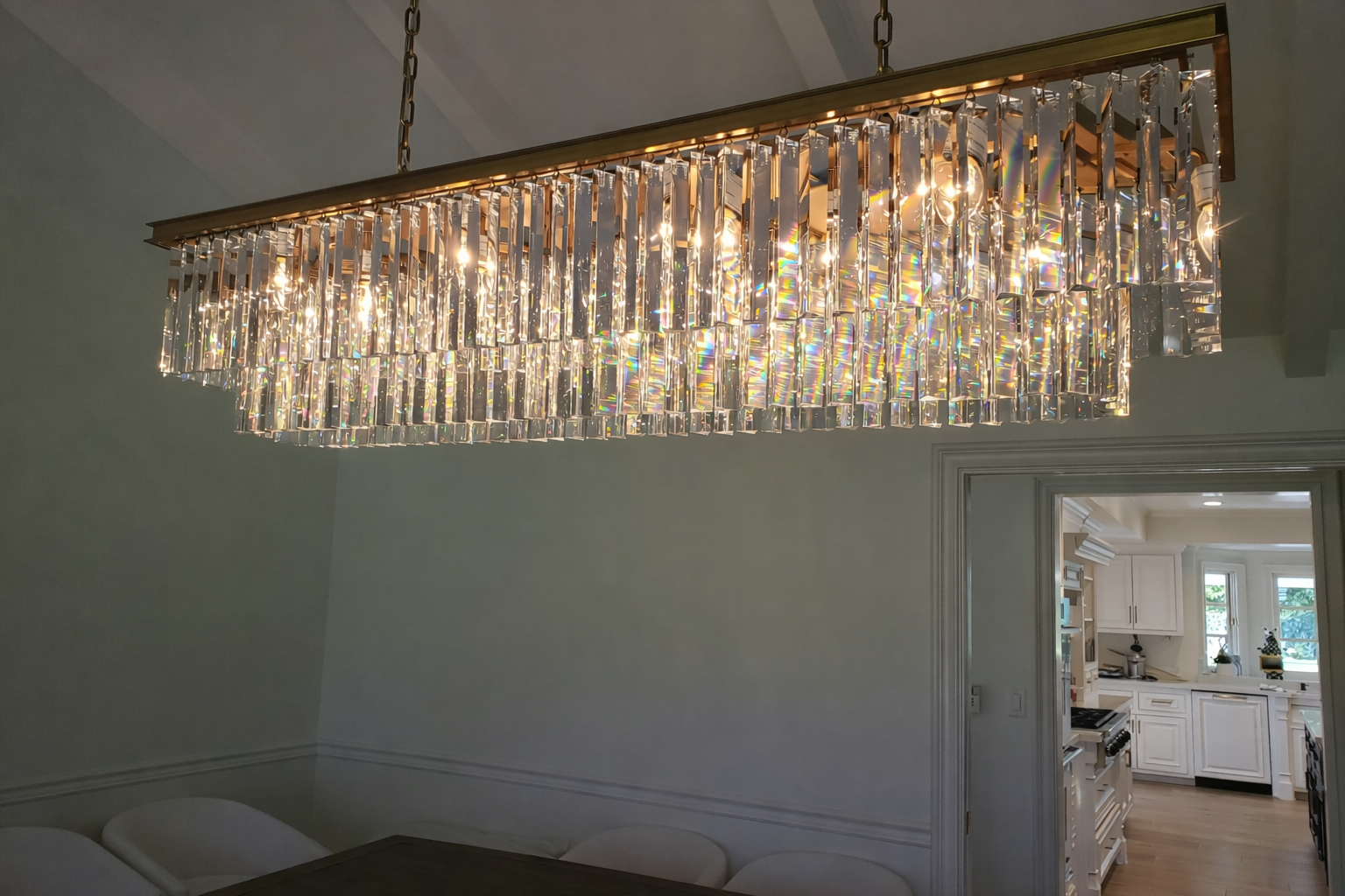 A luxurious rectangular chandelier with hanging crystals, installed above a dining table in a home interior.