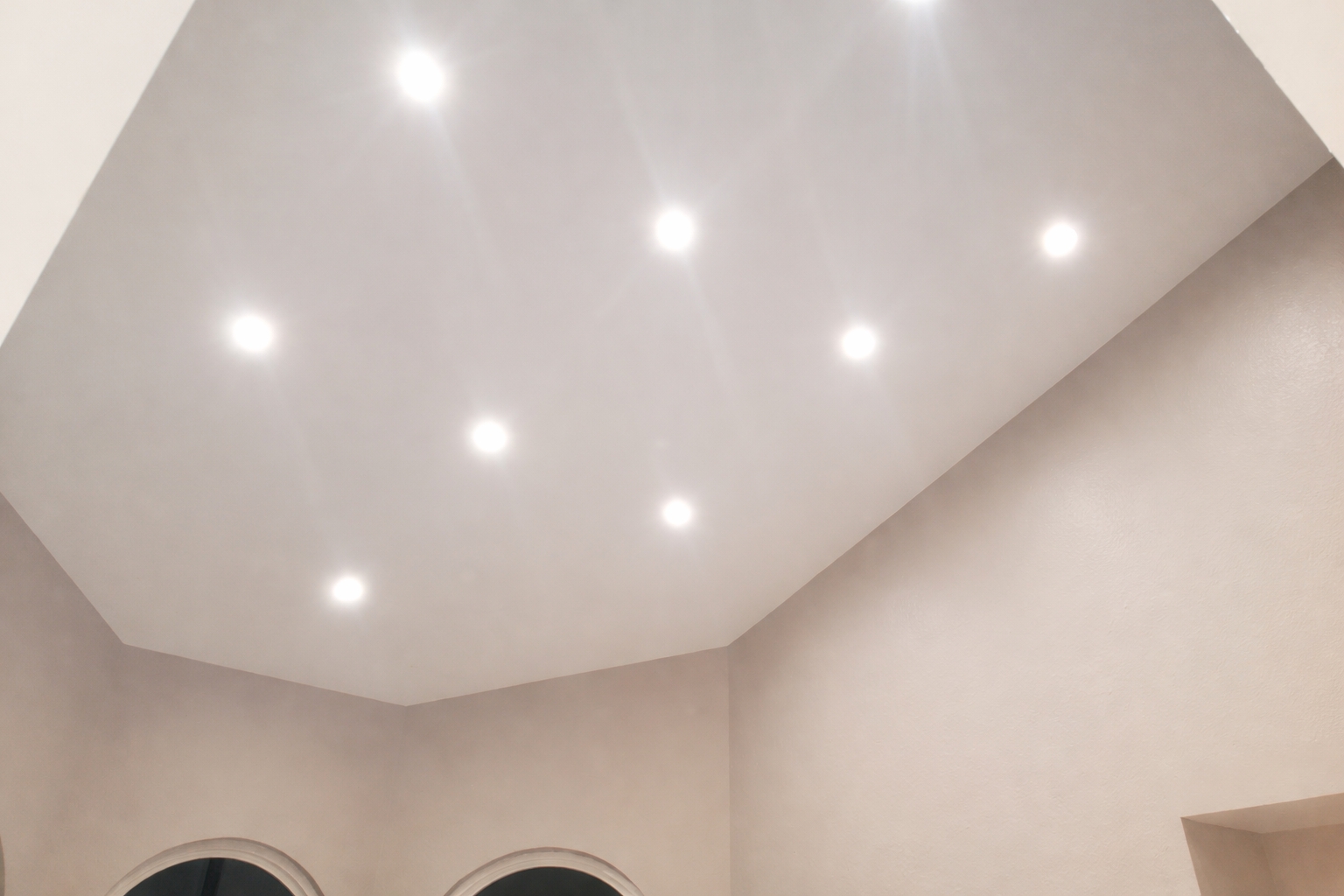 Ceiling with six recessed lights in a room with beige walls and an arched window.