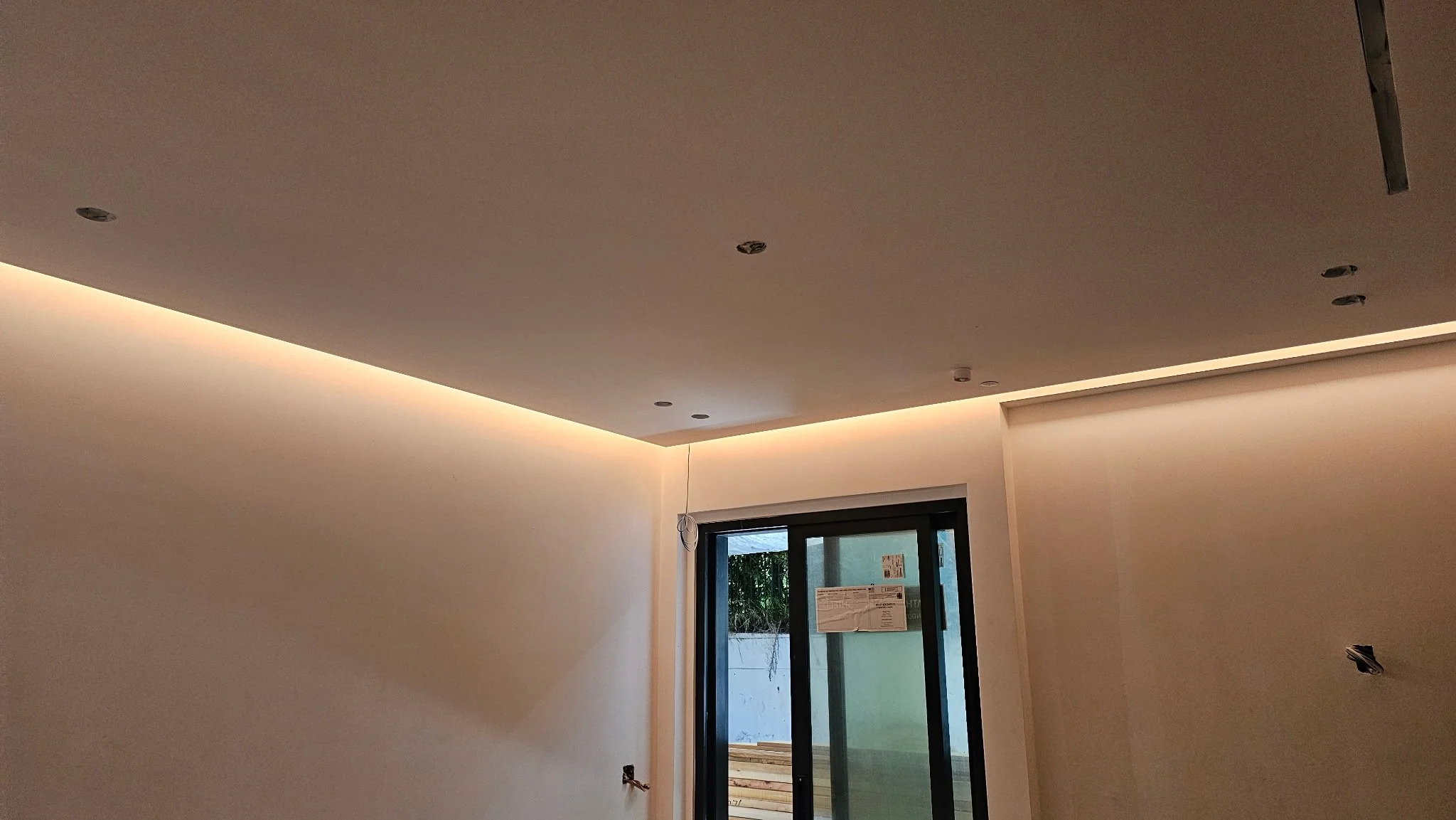 Interior of a modern room under construction with recessed lighting and a sliding glass door leading outside.
