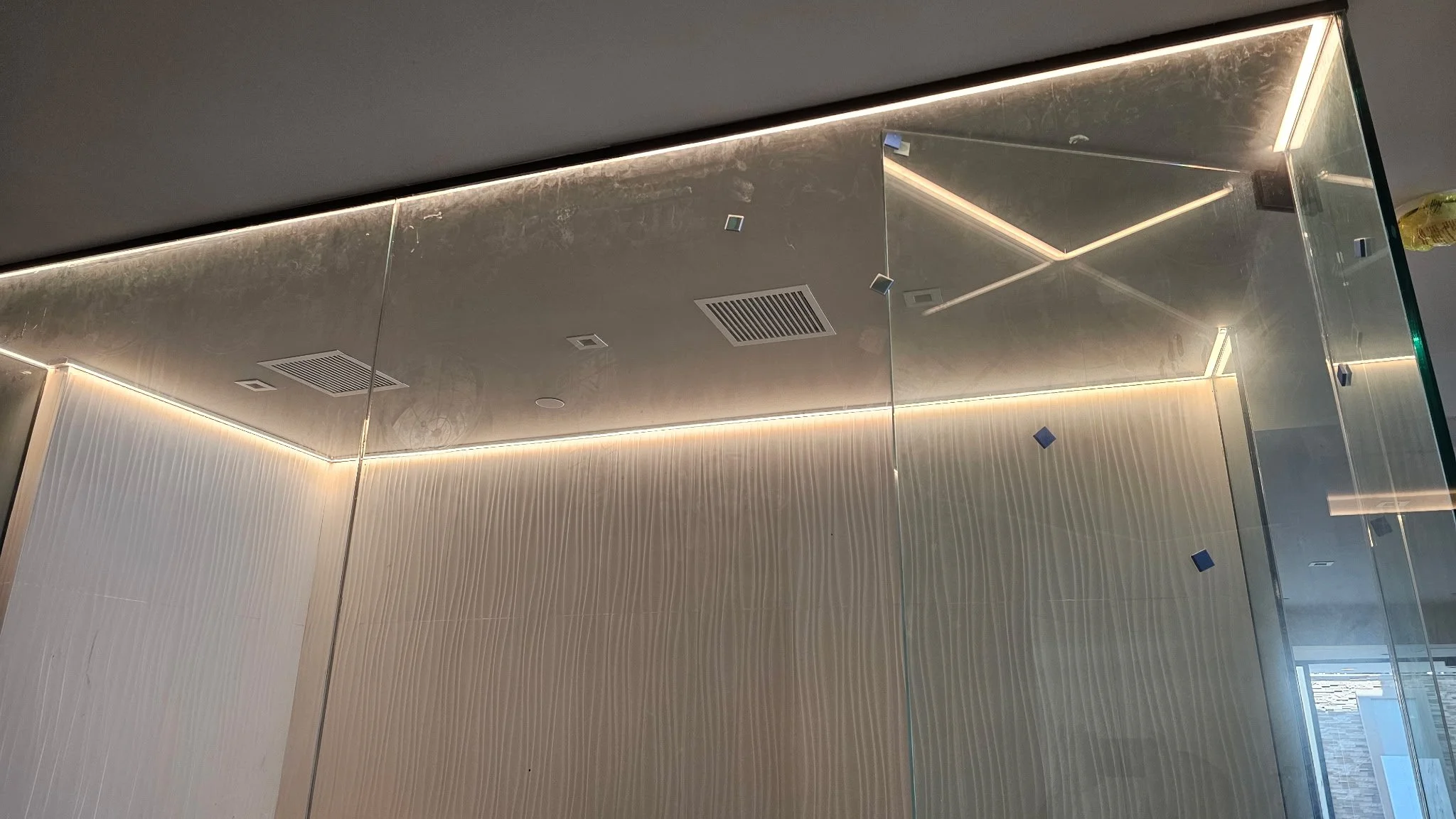 Interior ceiling with modern recessed lighting, air vents, and mirrored surfaces reflecting the room's design.