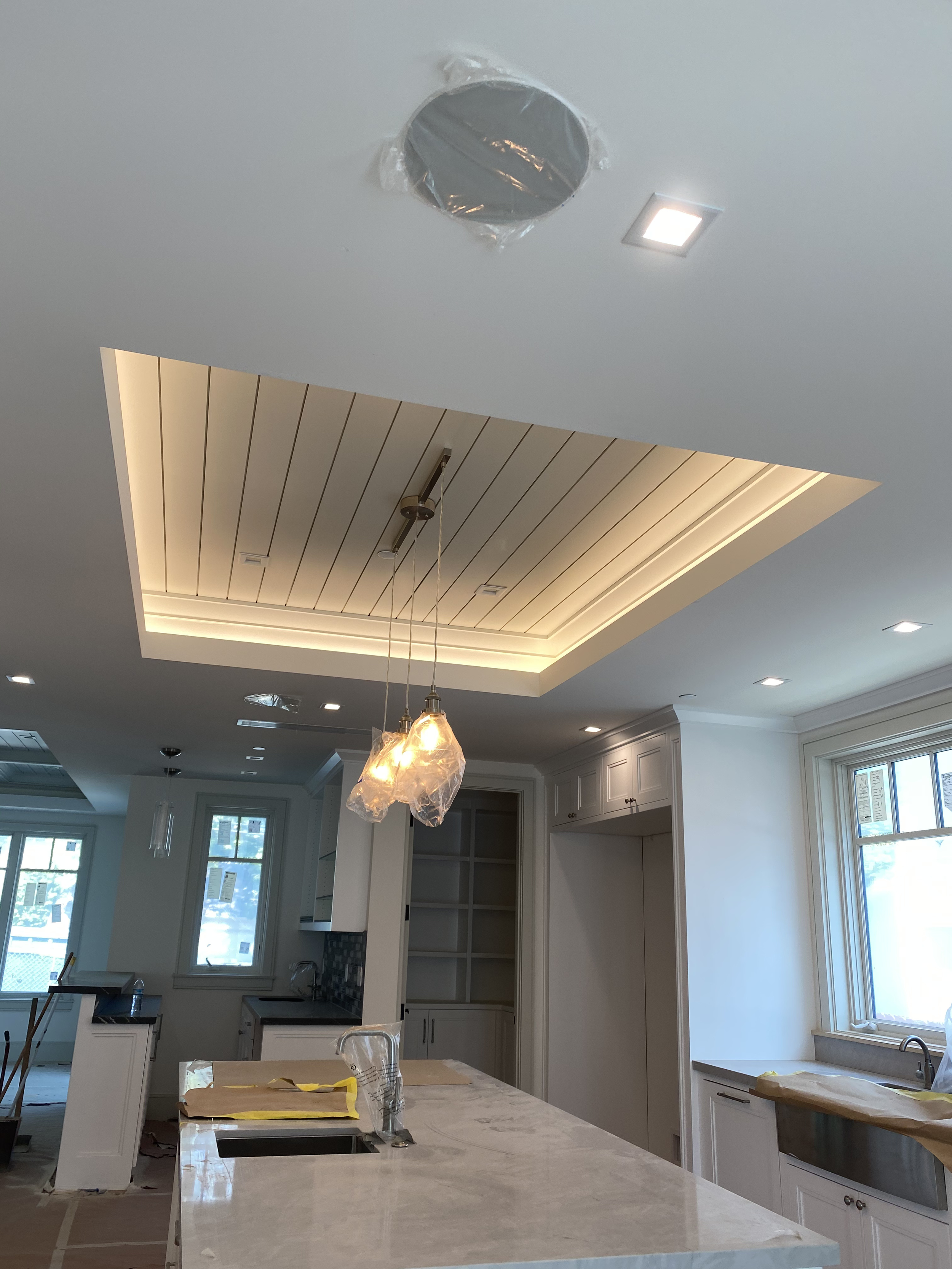 Modern kitchen under construction with a central island, built-in cabinets, large windows, and ceiling lighting fixtures.