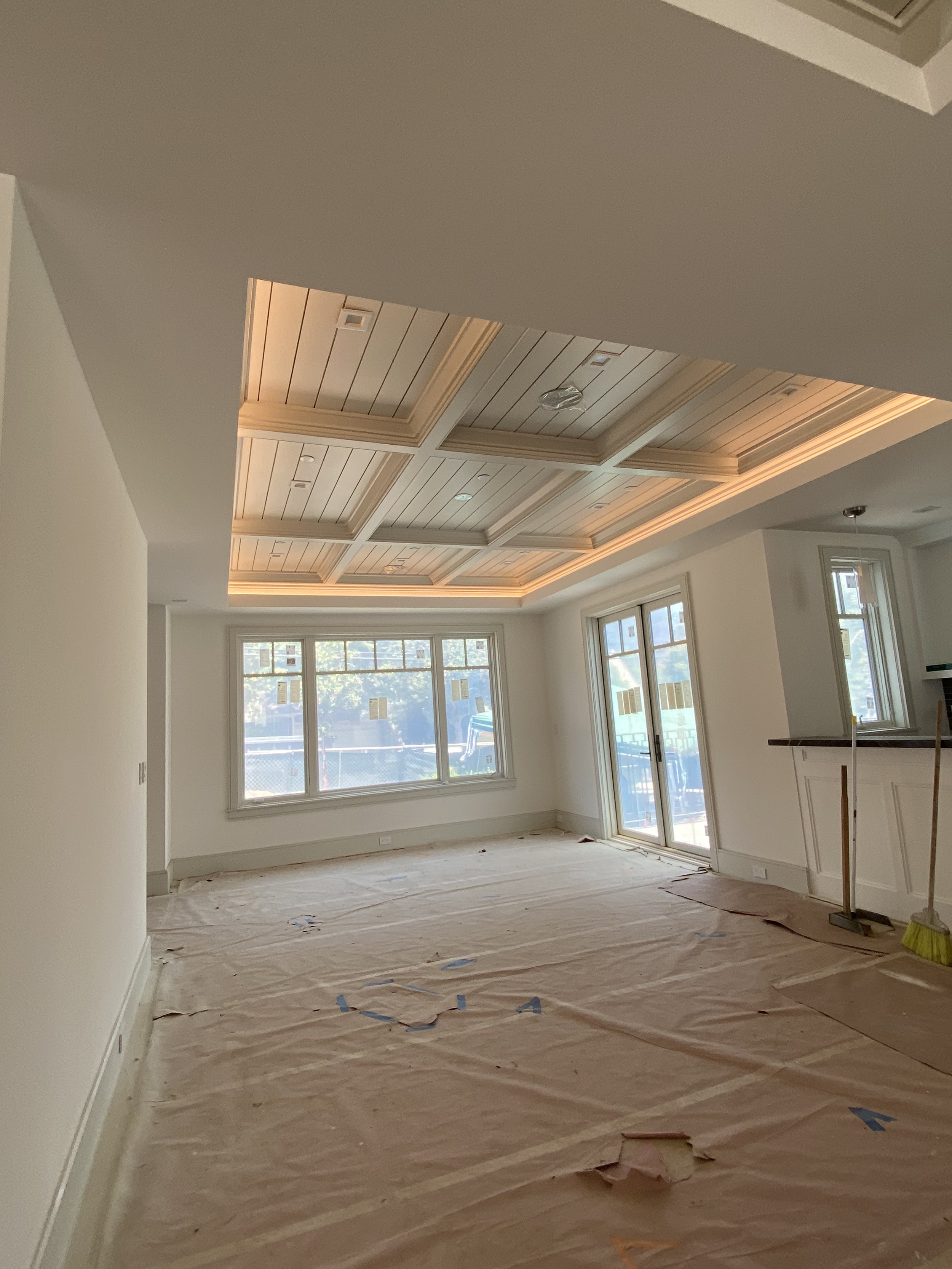 Empty living room with taped floor, large window, and a ceiling with wooden paneling and recessed lighting.