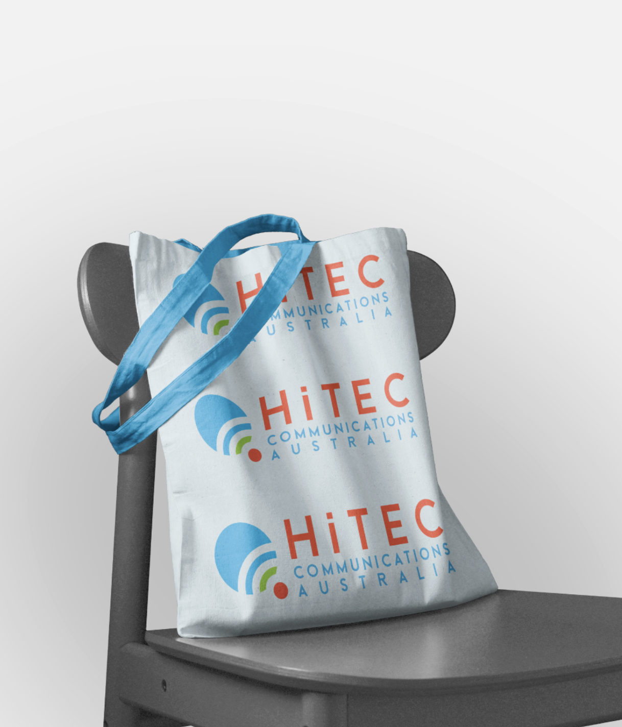 A tote bag with the logo of Hitec Communications Australia, placed on a chair with a gray background.