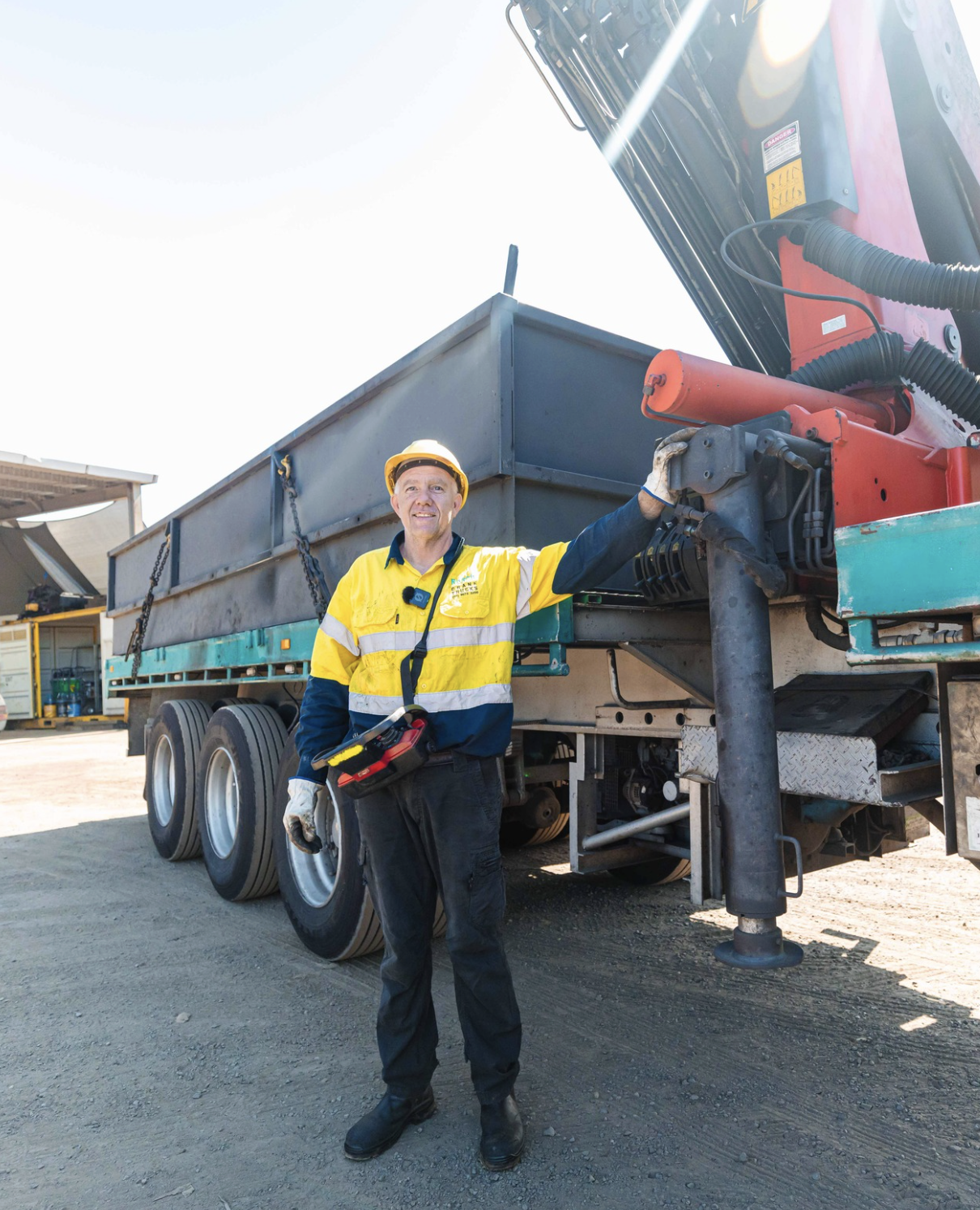 A construction worker in safety gear standing in front of a large construction vehicle, smiling at the camera.