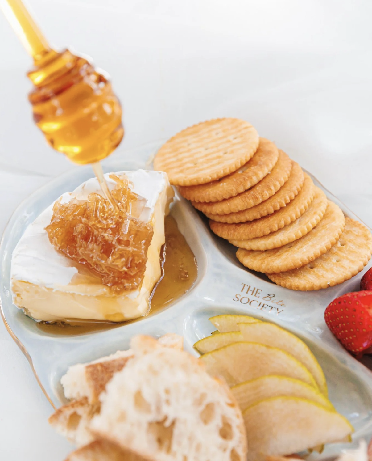 A cheese board with honey, crackers, strawberries, and lemon slices.