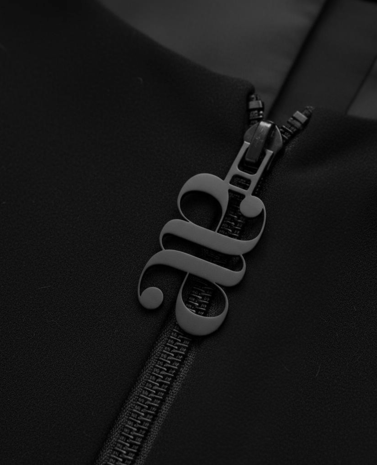 A close-up view of a black zipper with a white treble clef-shaped zipper pull on a dark fabric surface.