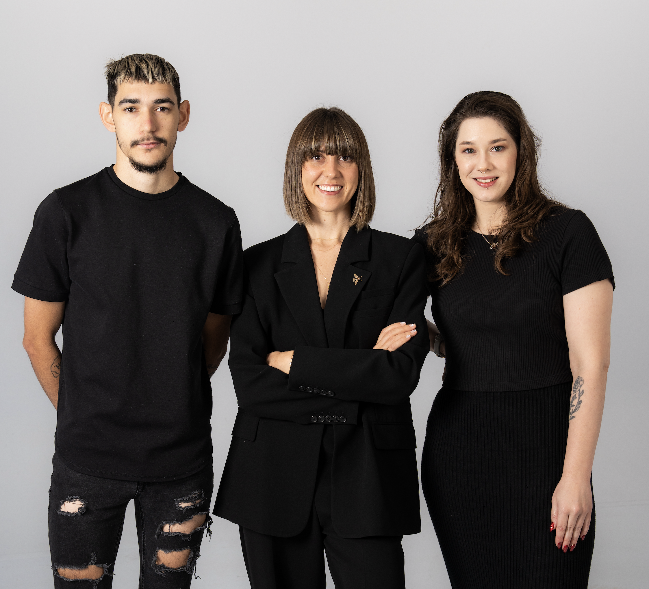 Three people standing together against a plain gray background, smiling and looking at the camera.