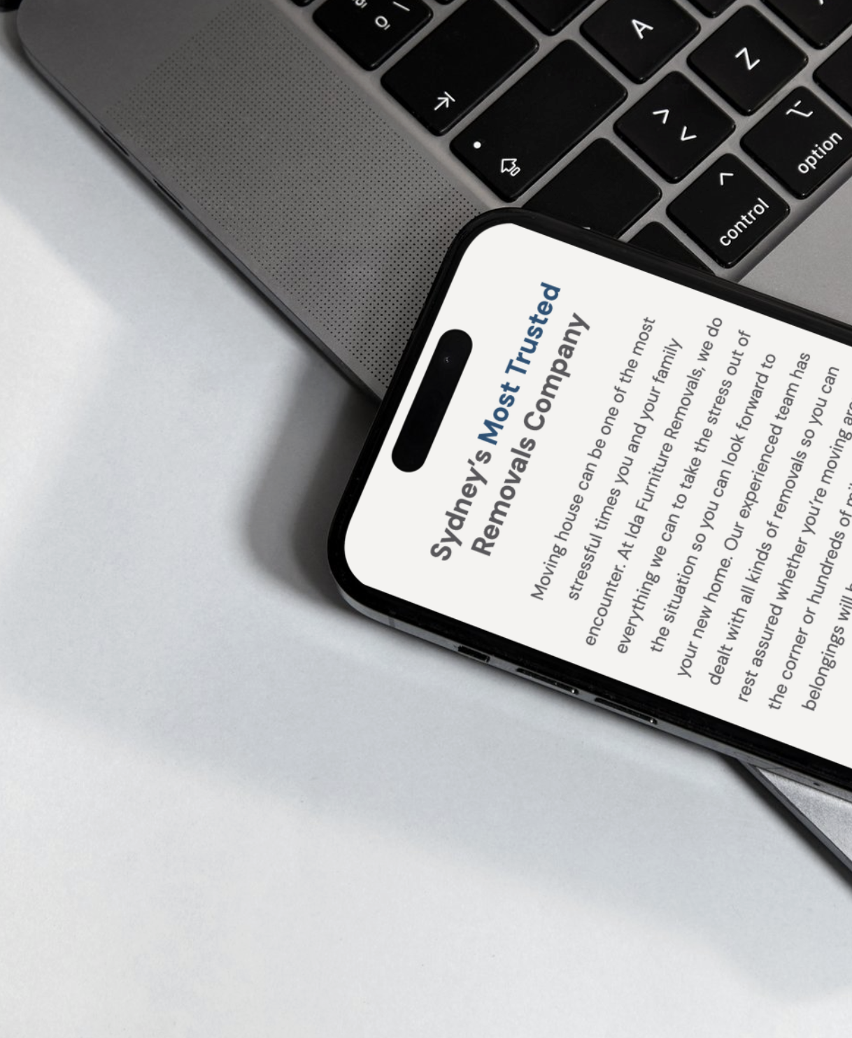 Close-up of a smartphone displaying a text about Sydney's Most Trusted Removals Company, placed on a white surface next to a laptop keyboard.