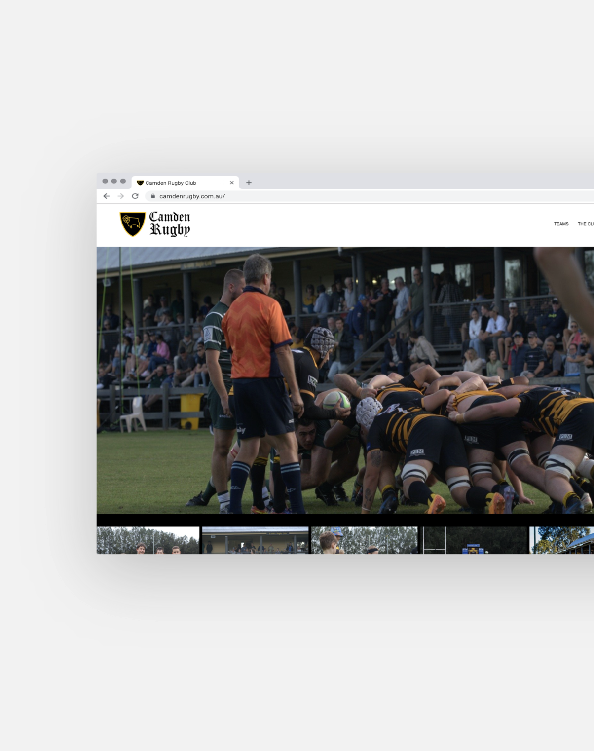 A rugby match with players in black and yellow uniforms engaging in a scrum, officials in orange shirts, and spectators watching from stands.